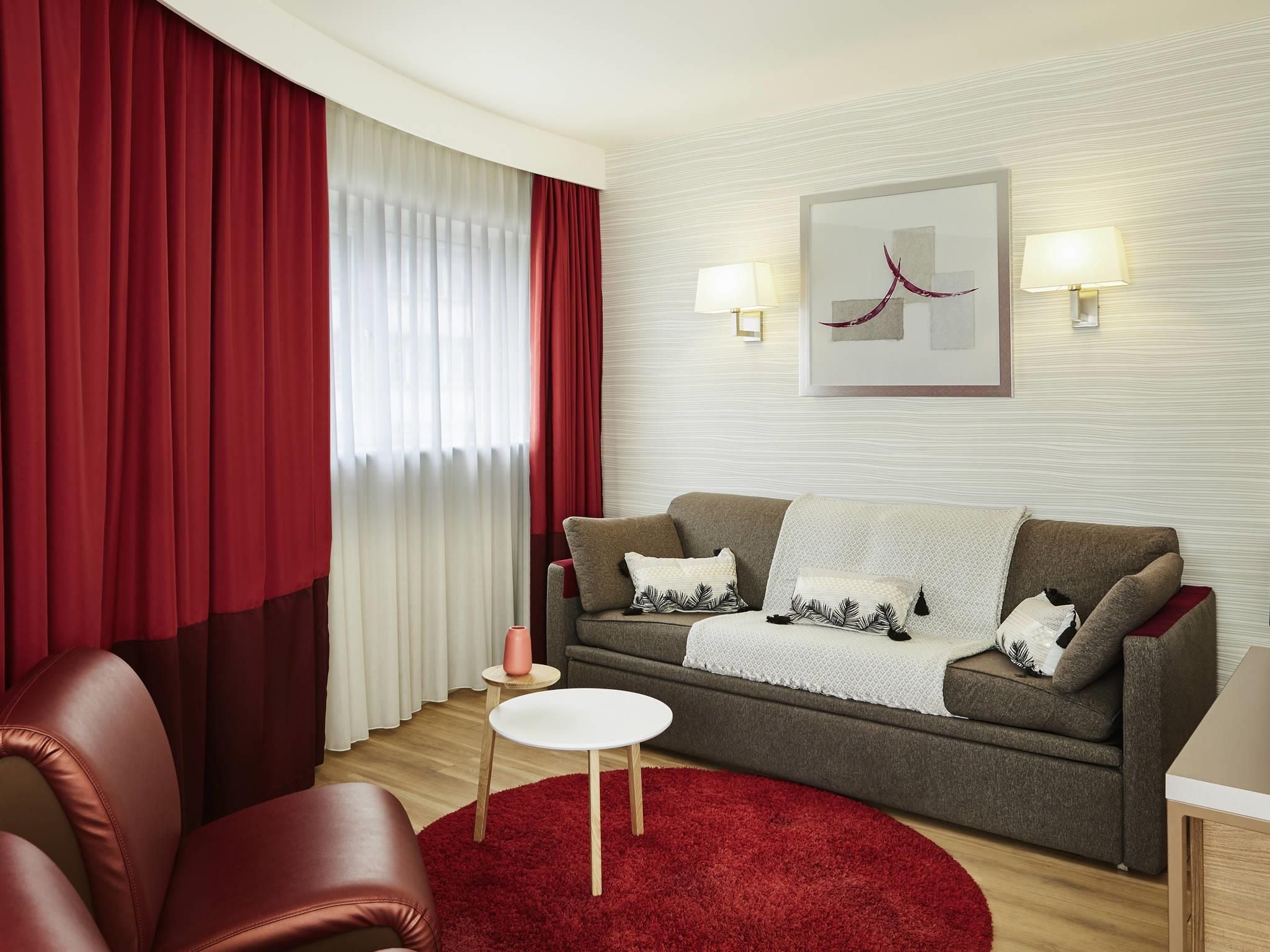 Un salon moderne avec un canapé gris, des rideaux rouges, une table blanche et un tapis rouge.