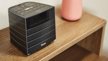 A black iHome speaker on a wooden shelf with a pink vase in the background.
