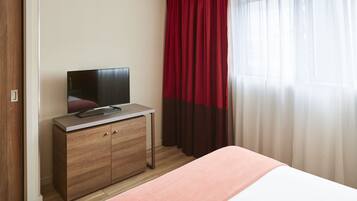 A hotel room with a bed, a TV on a wooden cabinet, and red curtains.