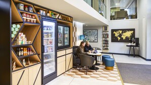 Un interior moderno con una zona de cafetería, que incluye un refrigerador lleno de bebidas, un espacio de estar con mesas y sillas, y un mapa mundial en la pared.