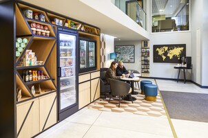 Un intérieur moderne comprenant un espace café, avec un réfrigérateur rempli de boissons, un coin salon avec des tables et des chaises, et une carte du monde accrochée au mur.