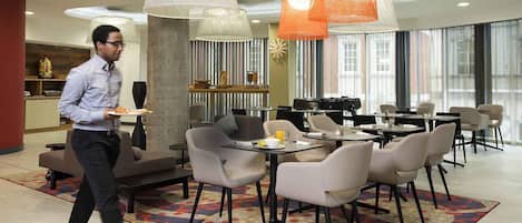 Un espace de restauration moderne offrant différents types de sièges, notamment des tables rondes et des canapés, ainsi qu’un tapis à motifs.