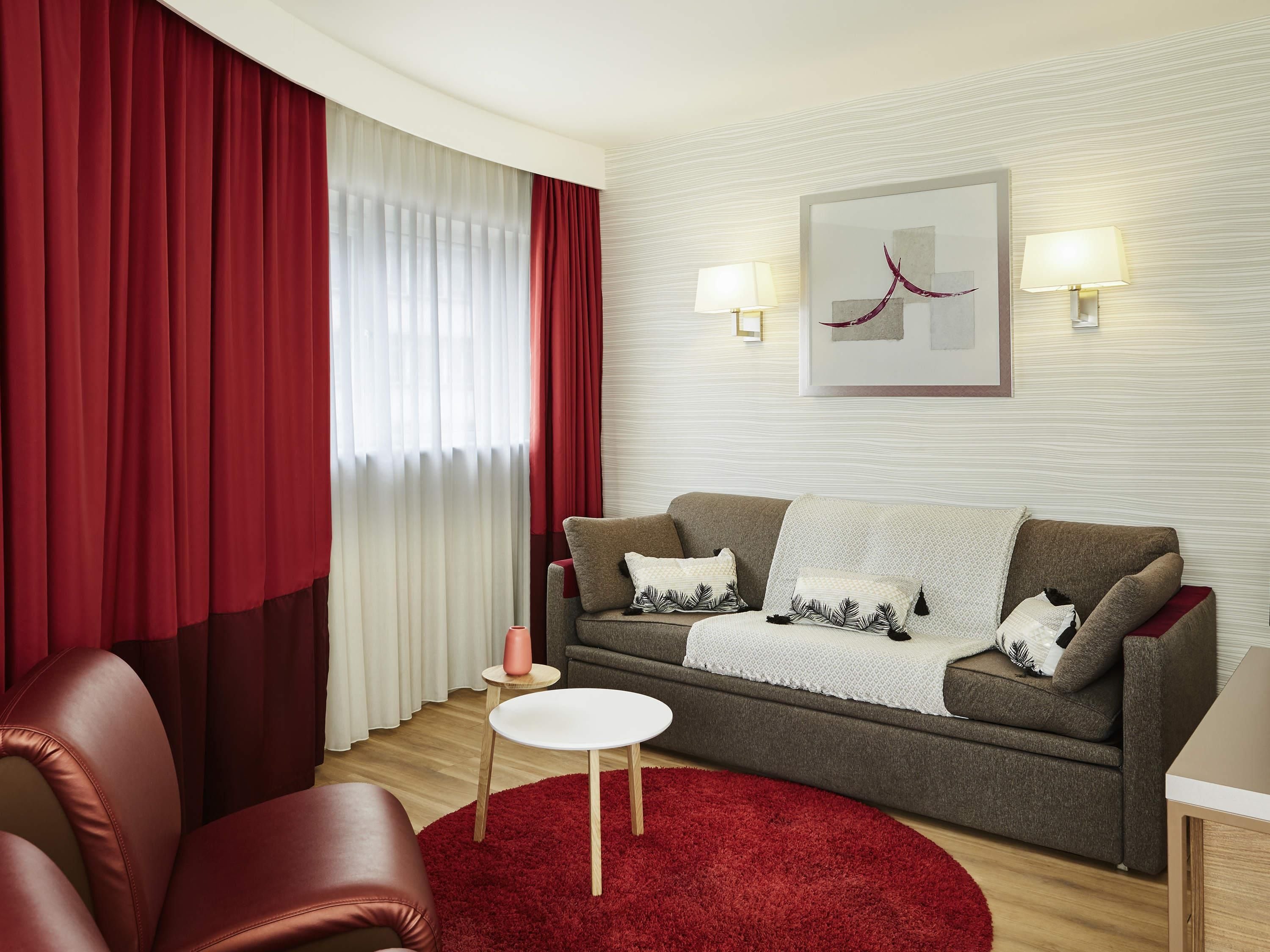 A modern living room with a grey sofa, red curtains, a red rug, and two wall-mounted lamps.