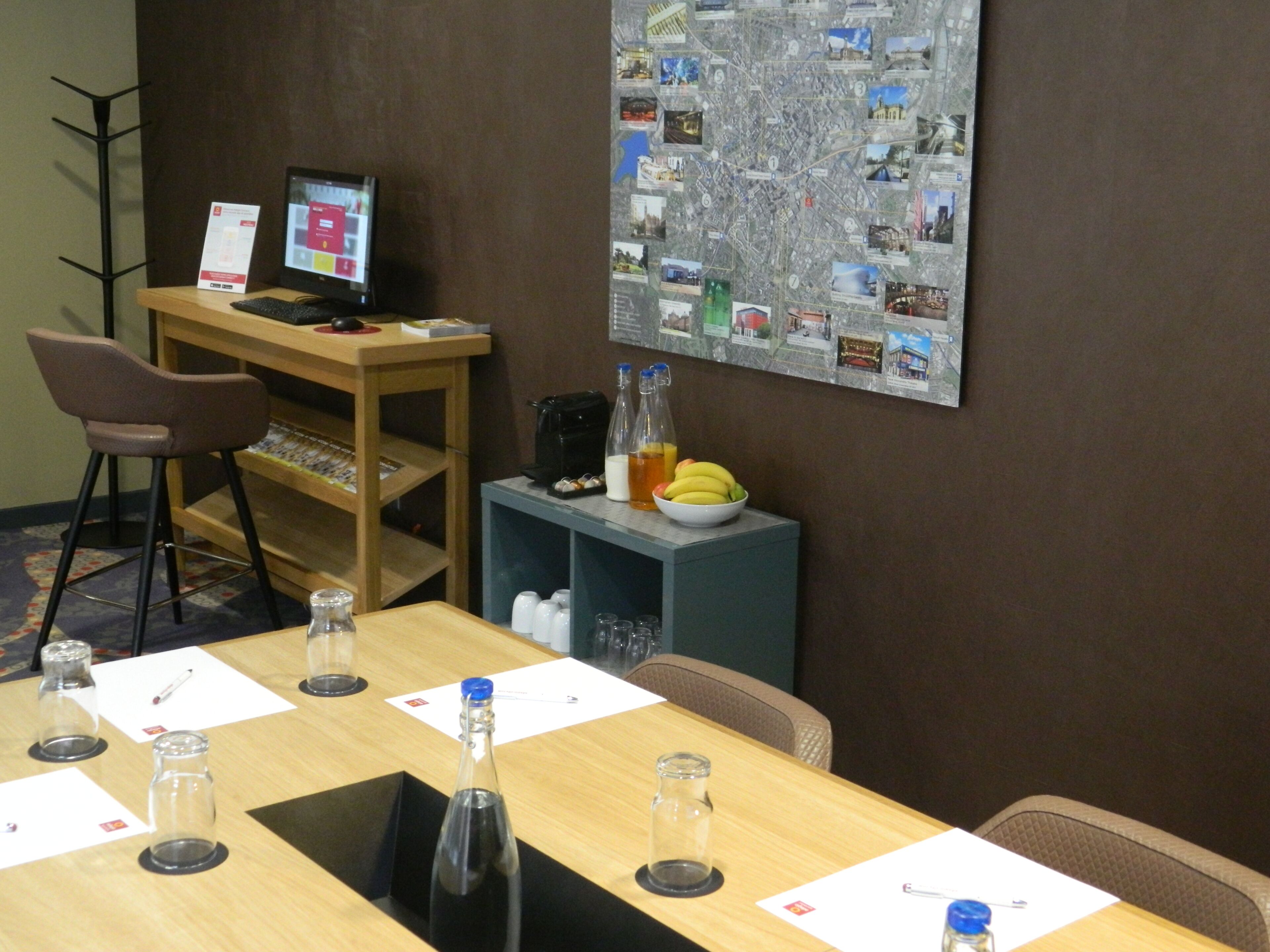 A conference room with a wooden table, chairs, a computer, a map on the wall, and a bowl of fruit.