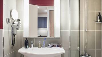 A bathroom with a sink, mirror, hairdryer, and shower.