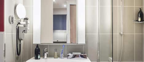 A bathroom with a sink, mirror, hairdryer, and shower.