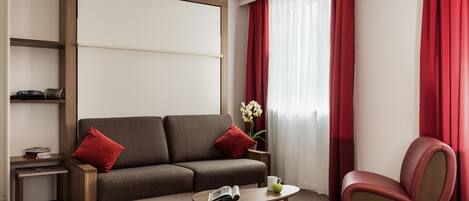 Een moderne woonkamer met een bank, een salontafel, een rode fauteuil en een boekenkast.