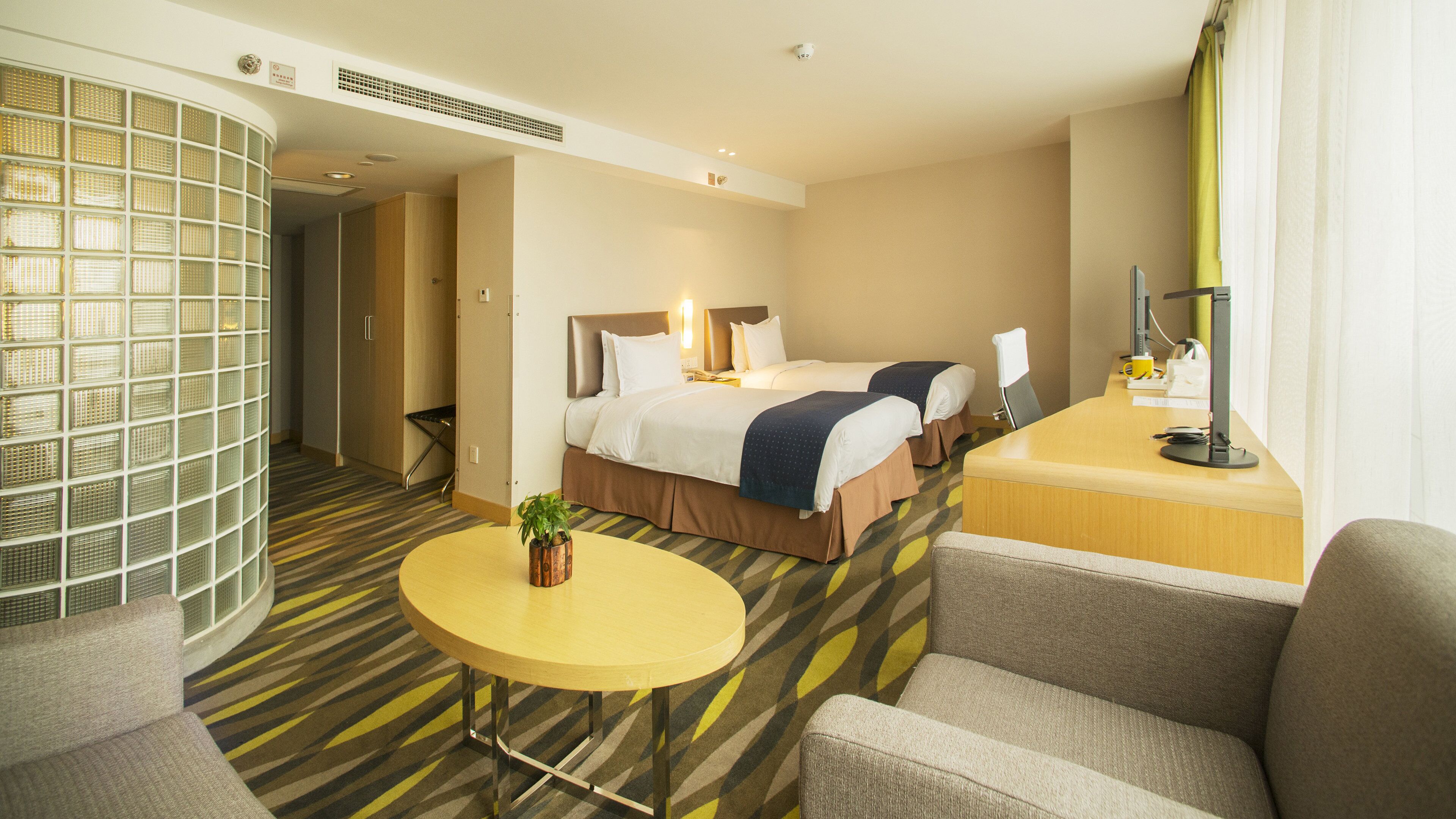 Une chambre d’hôtel avec un lit, un bureau, une chaise, une petite table et une plante en pot.