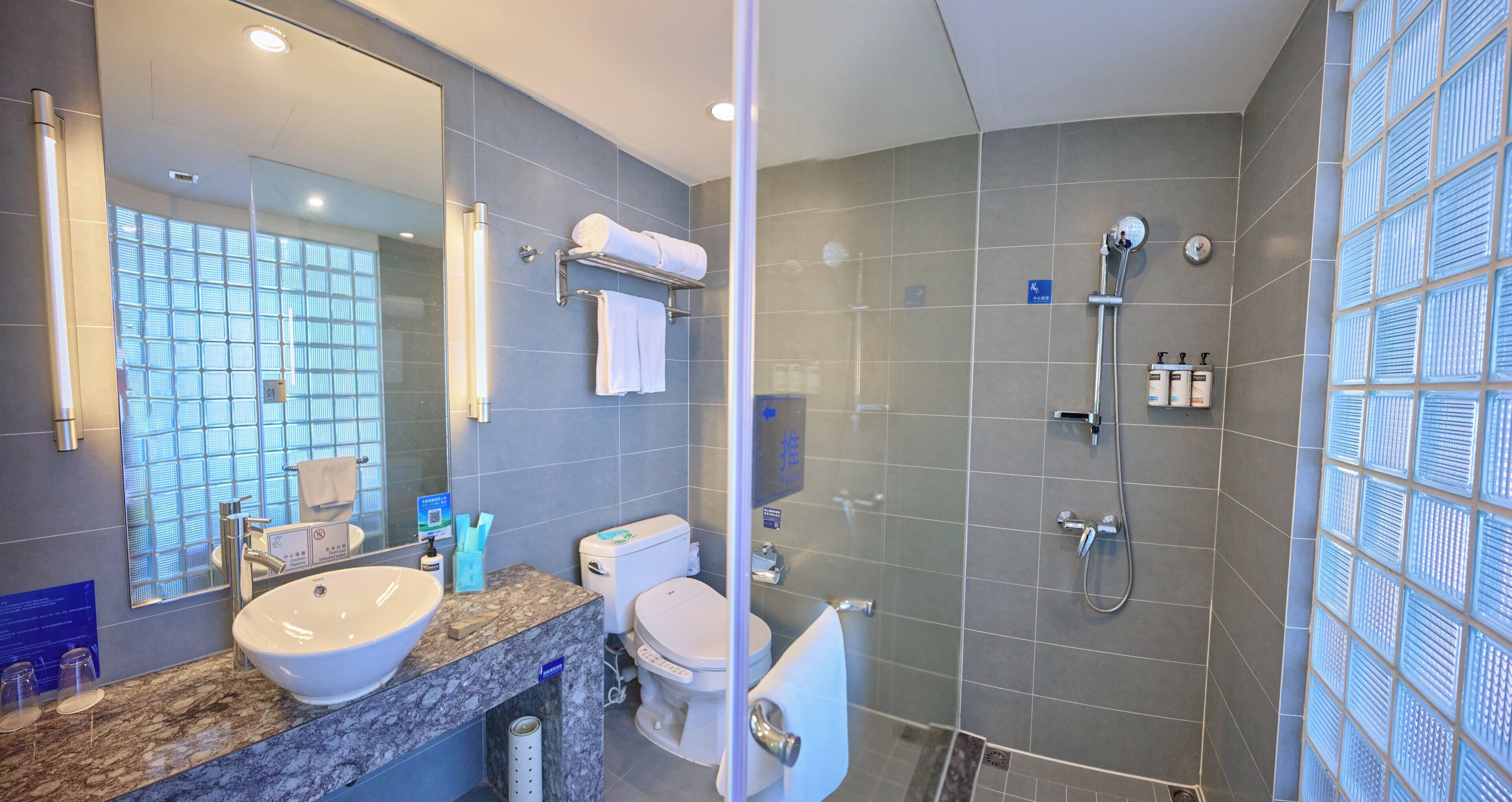 Un baño moderno con un espejo grande, un lavamanos, un inodoro y una zona de ducha.