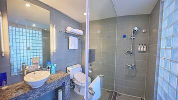 Un baño moderno con un espejo grande, un lavamanos, un inodoro y una zona de ducha.
