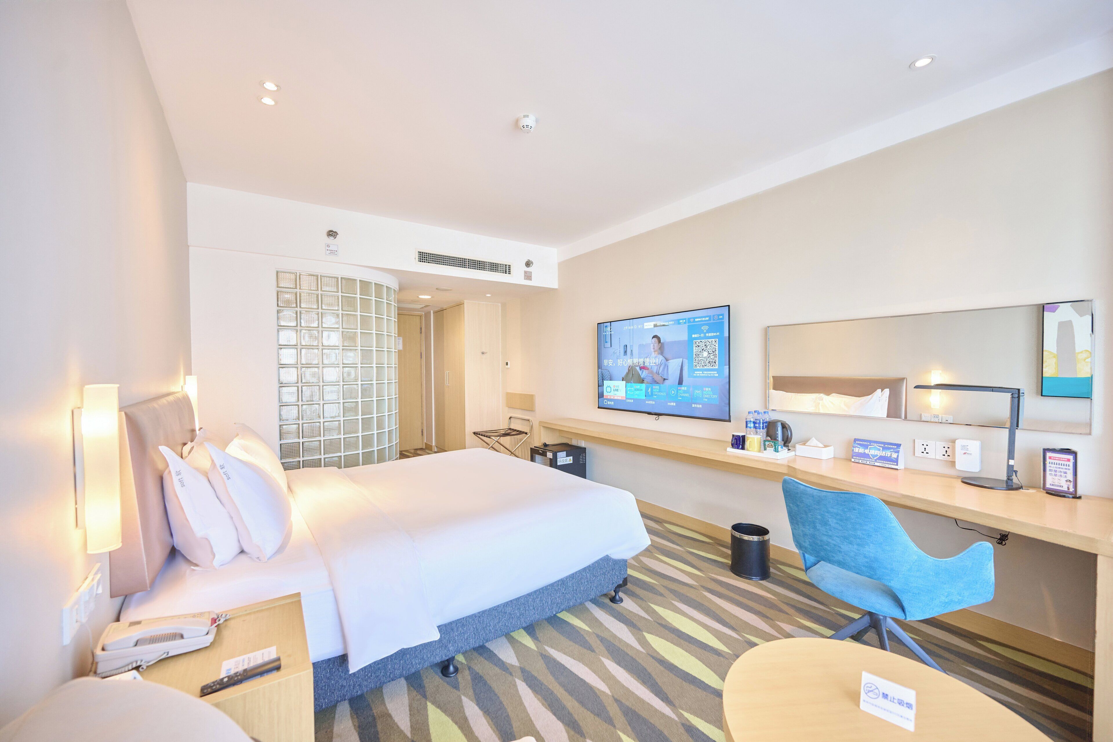 A hotel room with a bed, a desk with a computer, a chair, and a TV on the wall.