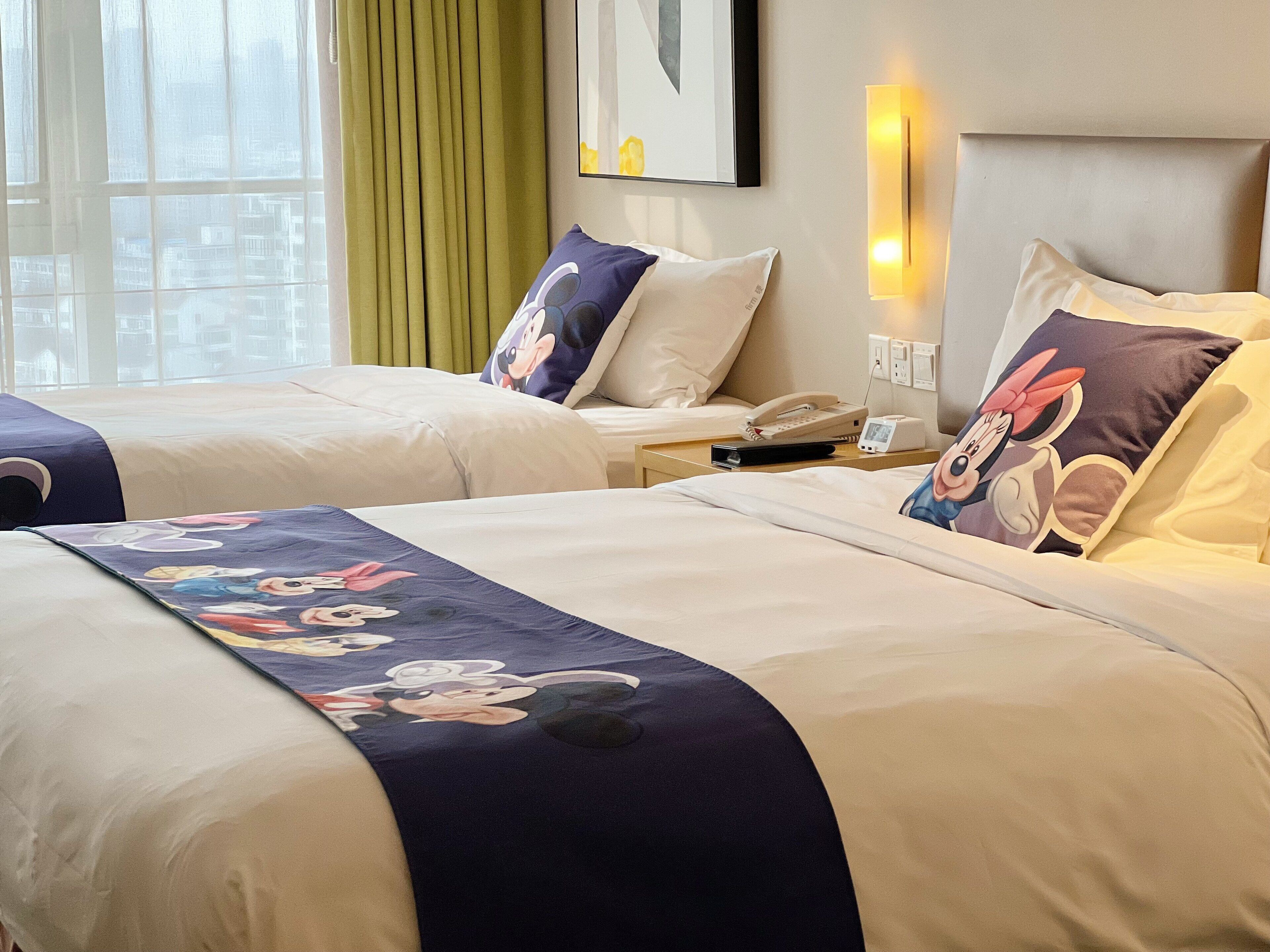 Habitación de hotel con dos camas, cada una con una colcha de temática de Mickey Mouse, un teléfono en la mesita de noche y una lámpara de pared.