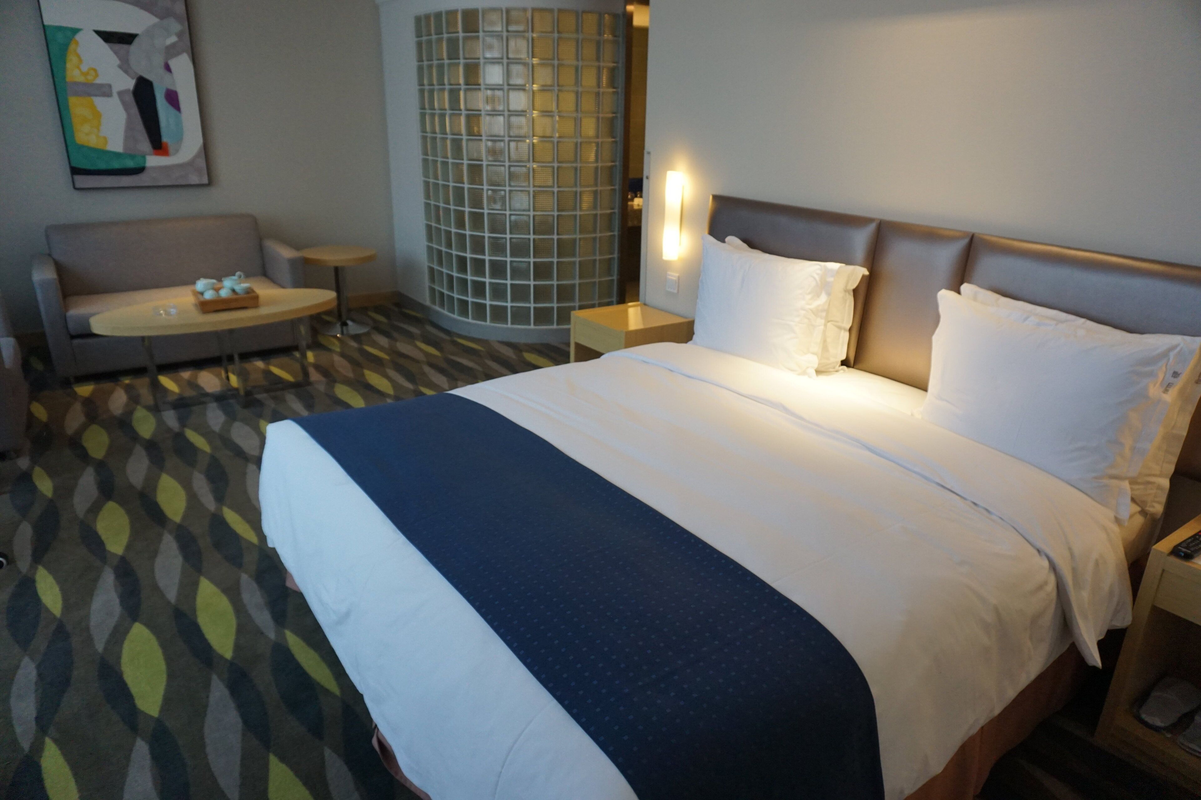 Habitación de hotel con una cama grande, un sofá, una mesita y una lámpara de pared.