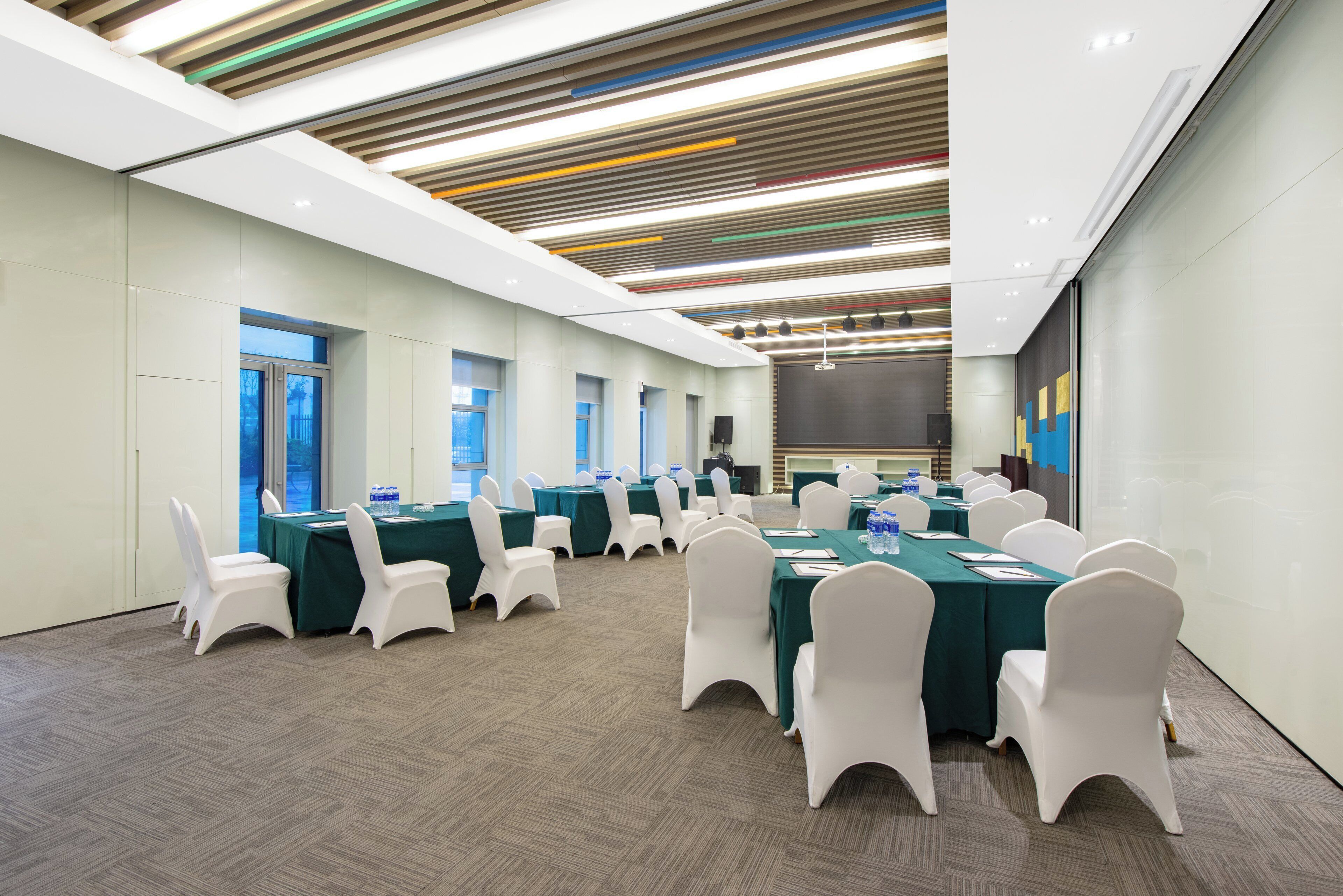 A conference room with multiple tables and chairs, large windows, and a modern ceiling design.