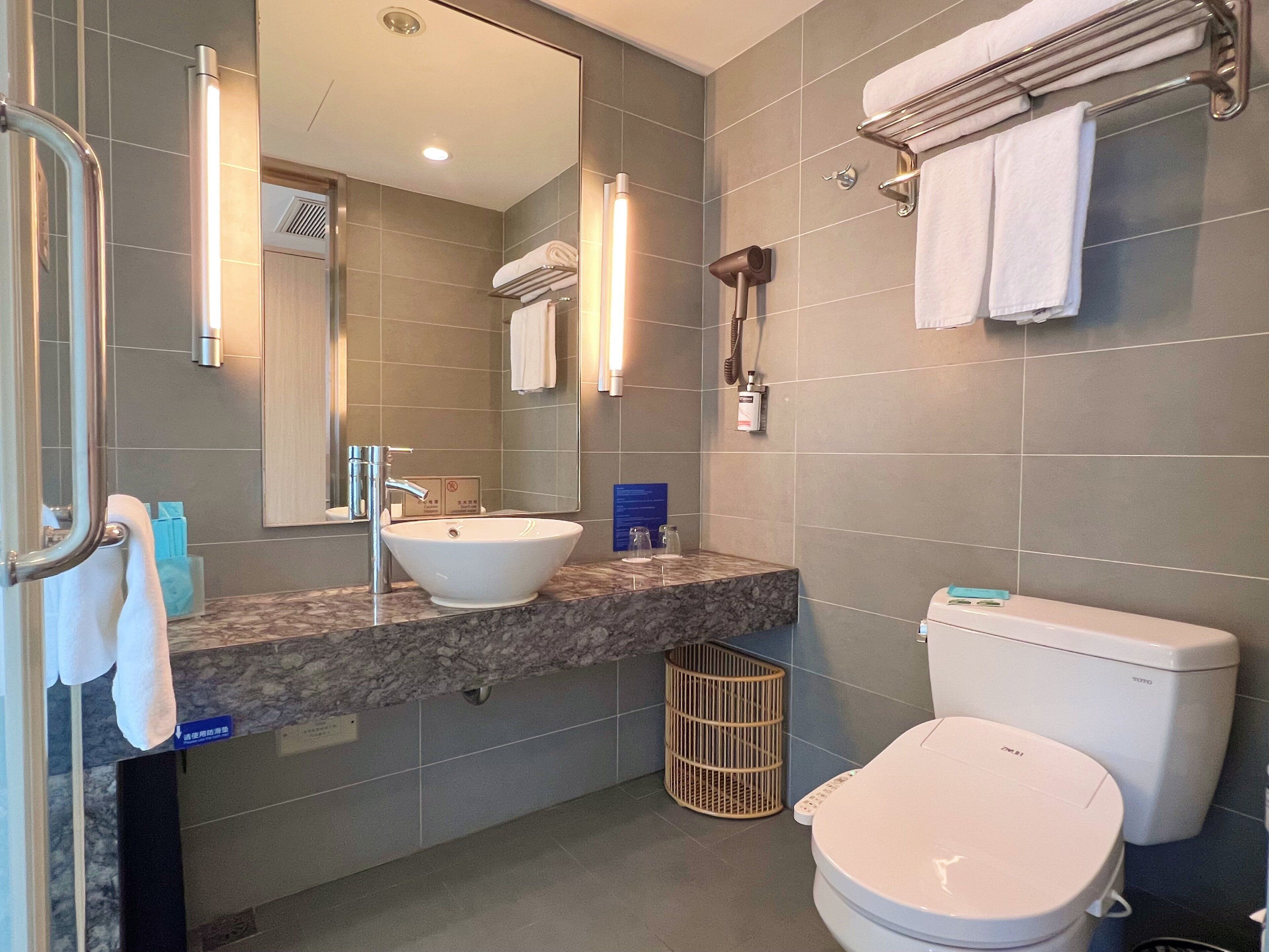 A modern bathroom with a sink, mirror, towel rack, and toilet.