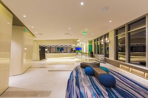 A modern hotel lobby with a reception desk, seating area, and a view of the dining area.