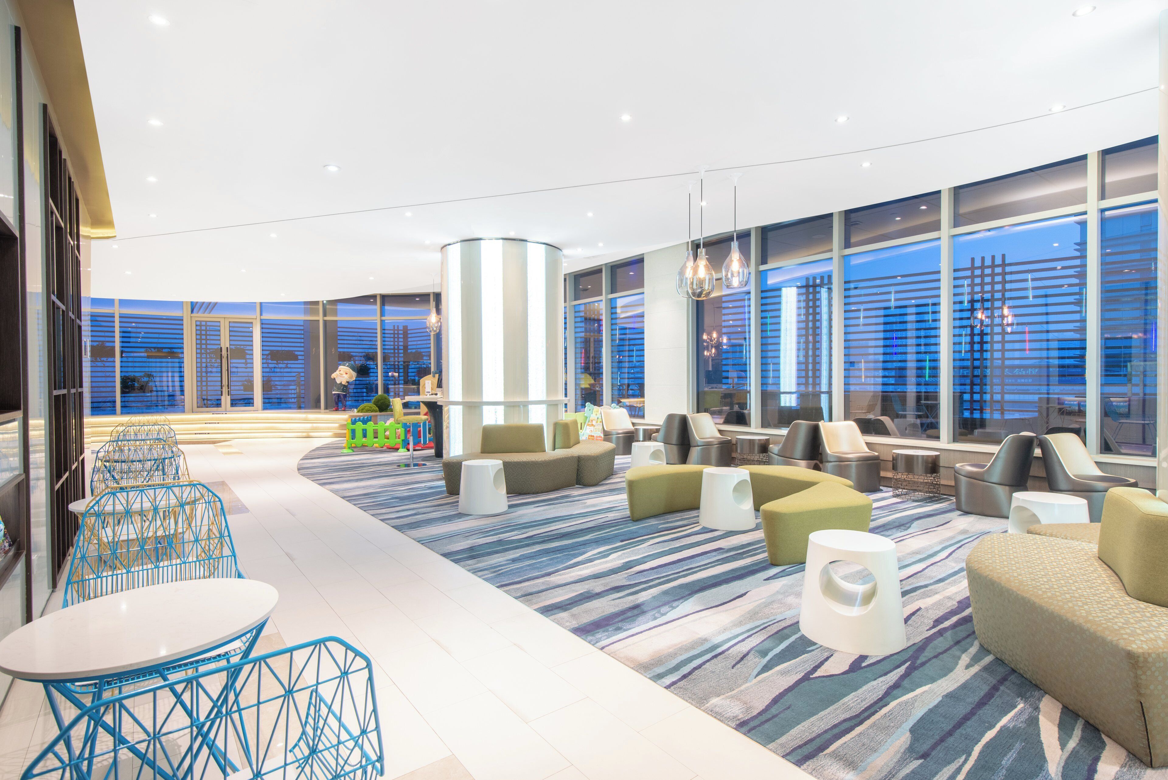 A modern lounge area with seating arrangements, a patterned carpet, and large windows offering views.