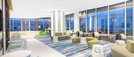 A modern lounge area with seating arrangements, a patterned carpet, and large windows offering views.