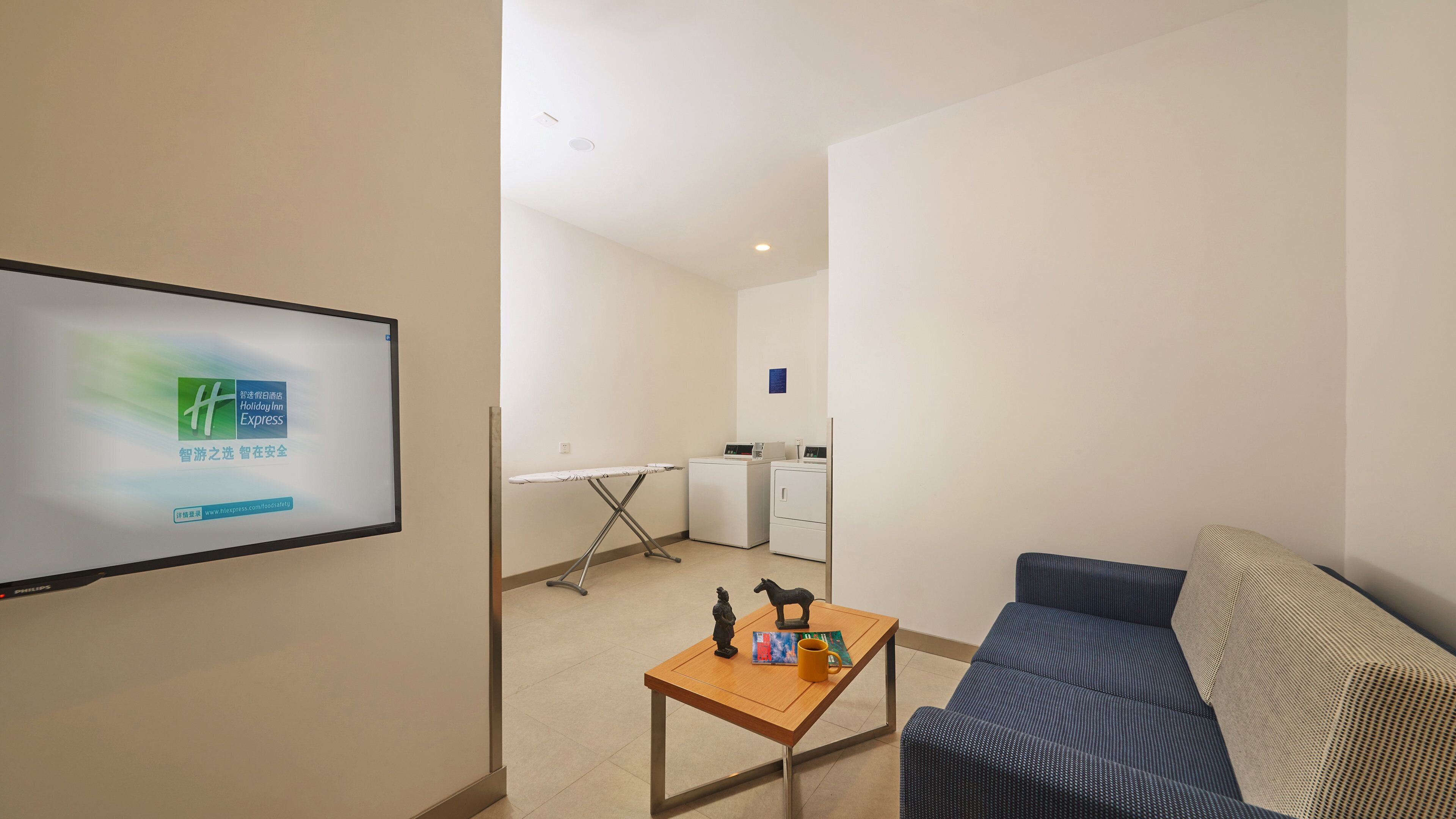 Une chambre d’hôtel équipée d’un téléviseur à écran plat, d’un canapé, d’une petite table avec une tasse à café, et d’un espace buanderie comprenant un lave-linge et un sèche-linge.