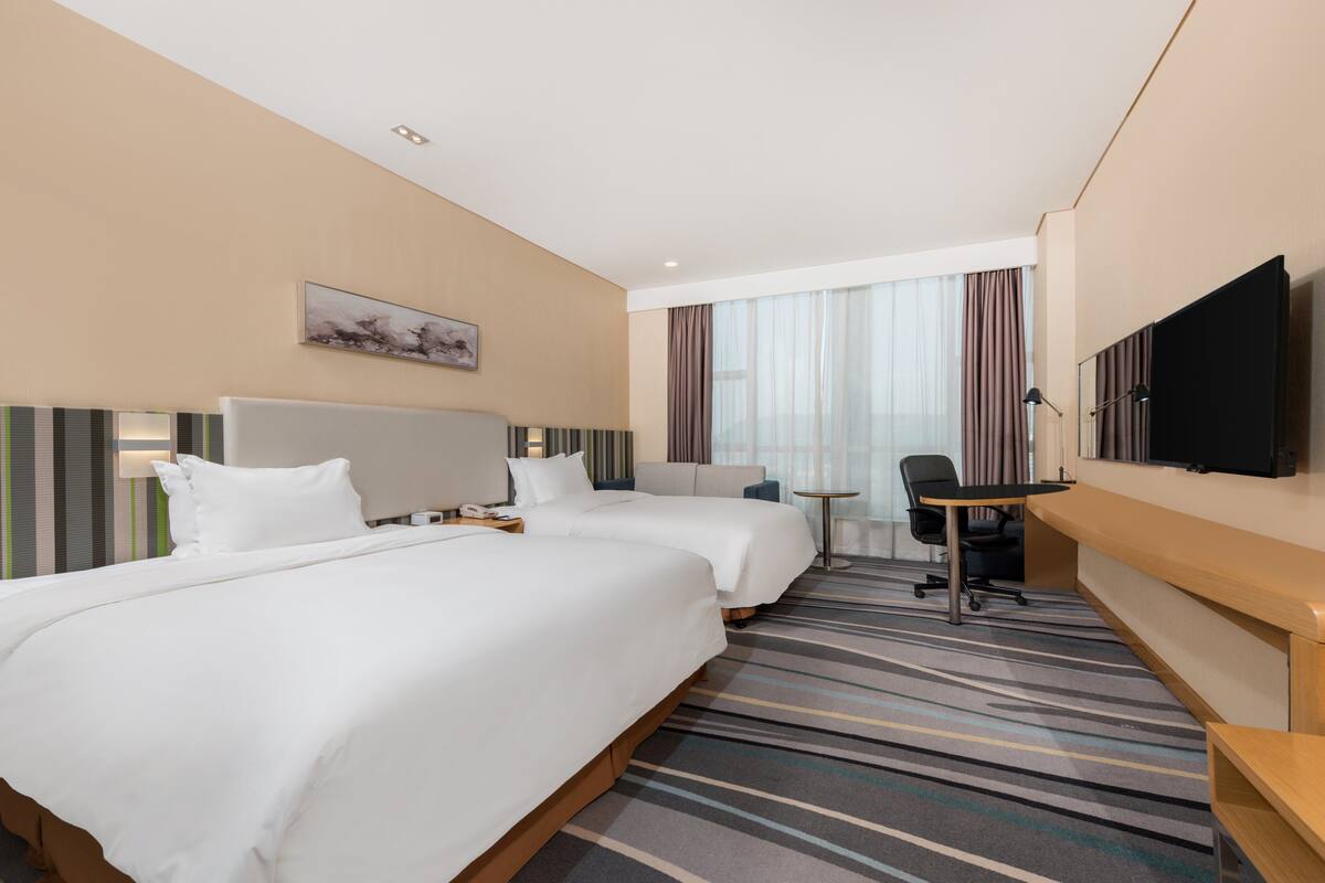 Une chambre d’hôtel avec deux lits, un bureau, une chaise, une télévision et une fenêtre avec des rideaux.
