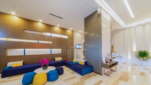 Eine moderne Hotelhalle mit Empfangstresen, einer Sitzecke mit bunten Kissen und einer großen Pflanze.