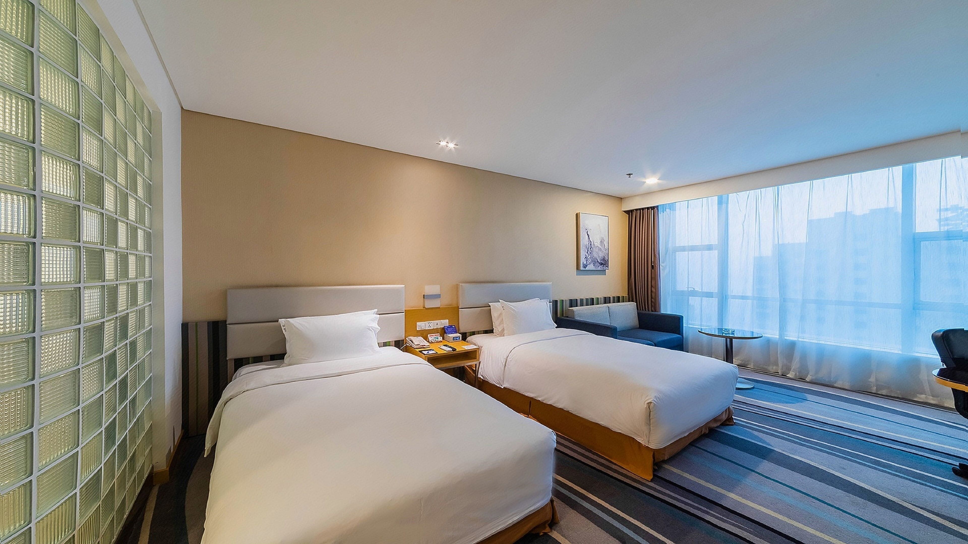 Une chambre d’hôtel avec deux lits, une petite table, une chaise et une grande fenêtre.