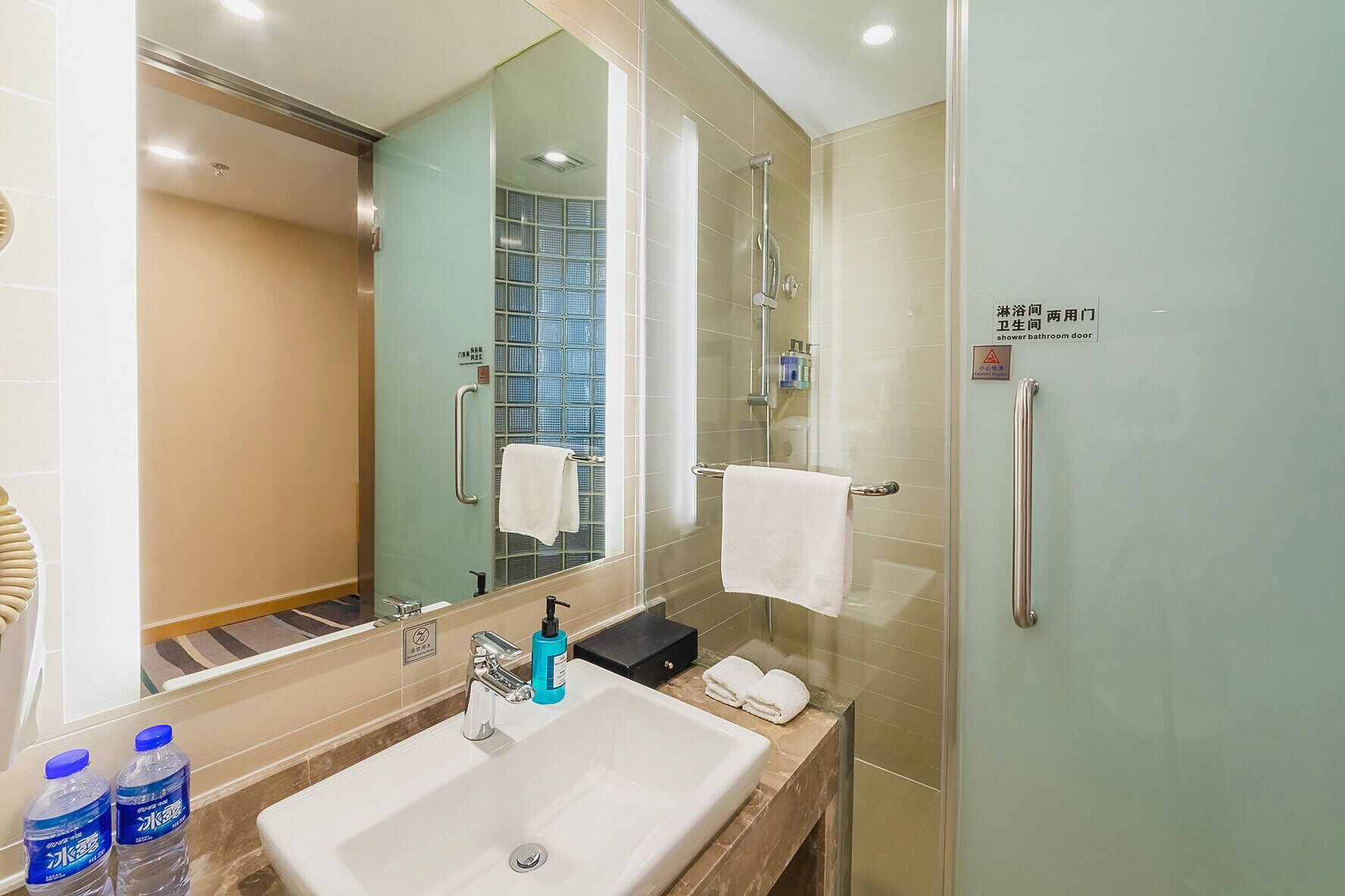 A modern bathroom with a large mirror, a sink, a glass shower enclosure, and a towel rack.