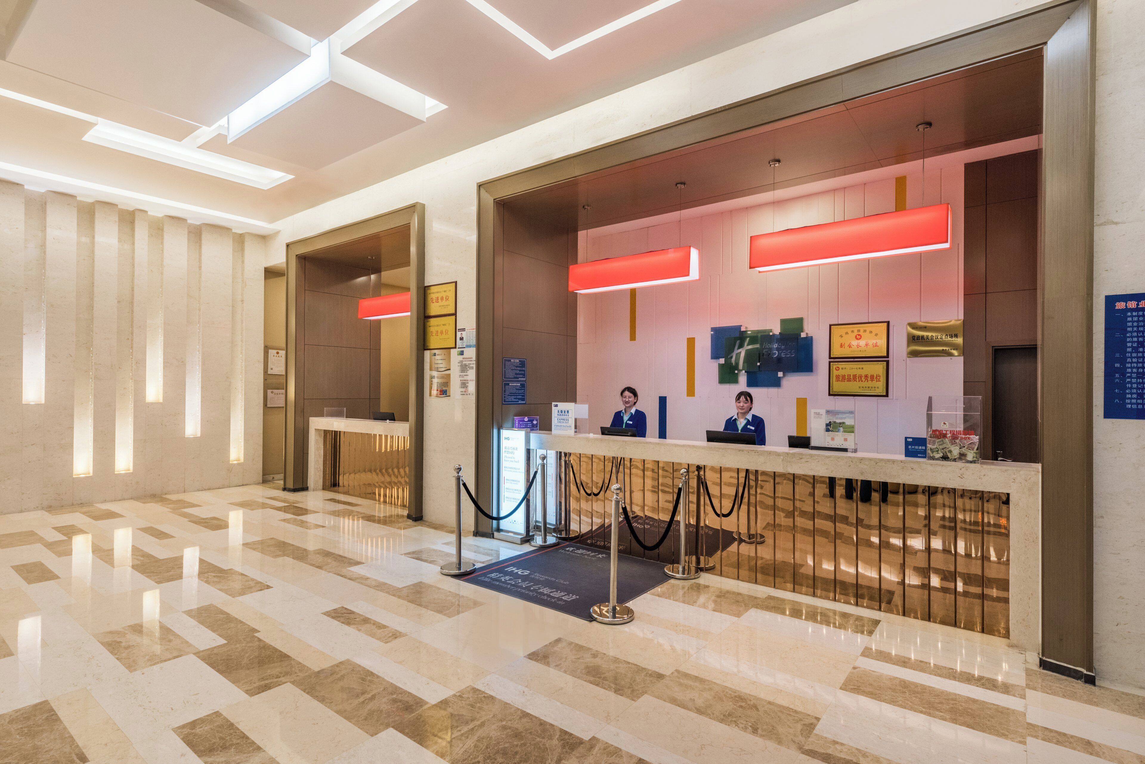 Zona de recepción de hotel con mostrador de registro, escritorio de recepción y área de espera con piso estampado.