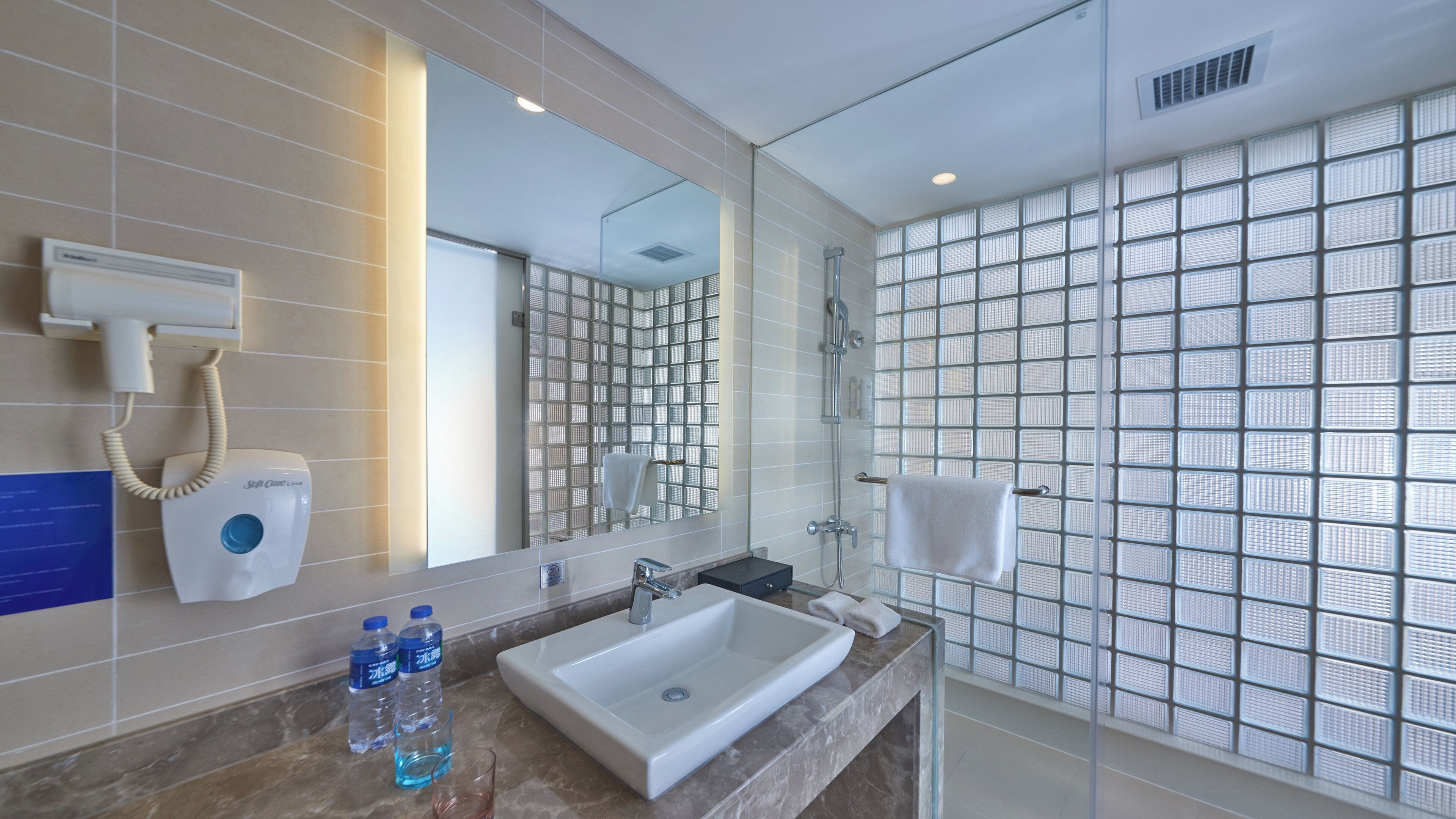 Un baño moderno con un espejo grande, un lavamanos, un secador de pelo y una cabina de ducha de vidrio.