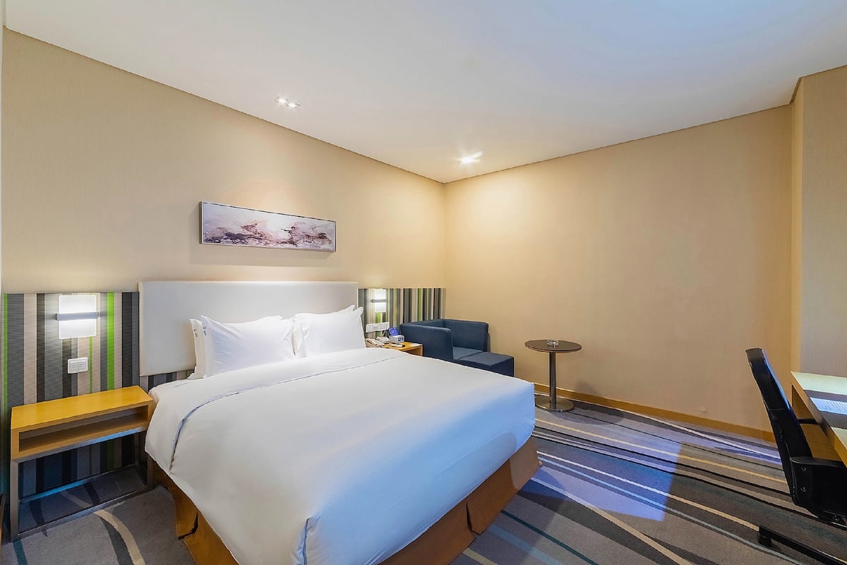 Une chambre d’hôtel avec un grand lit, un bureau, une chaise, une petite table et un téléviseur fixé au mur.