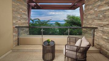 A balcony with a stone wall, a glass railing, a wicker chair, and a small table with a vase.
