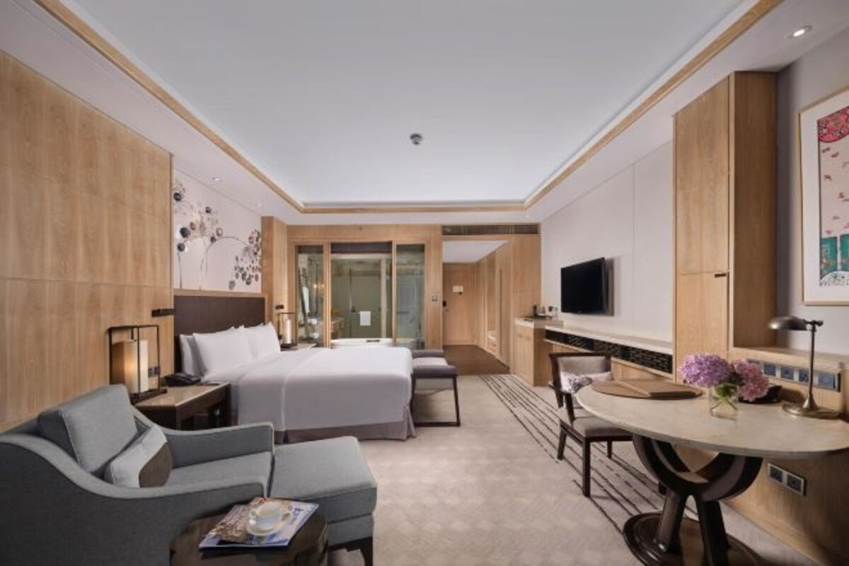 A modern hotel room with a bed, a sofa, a desk, and a TV.