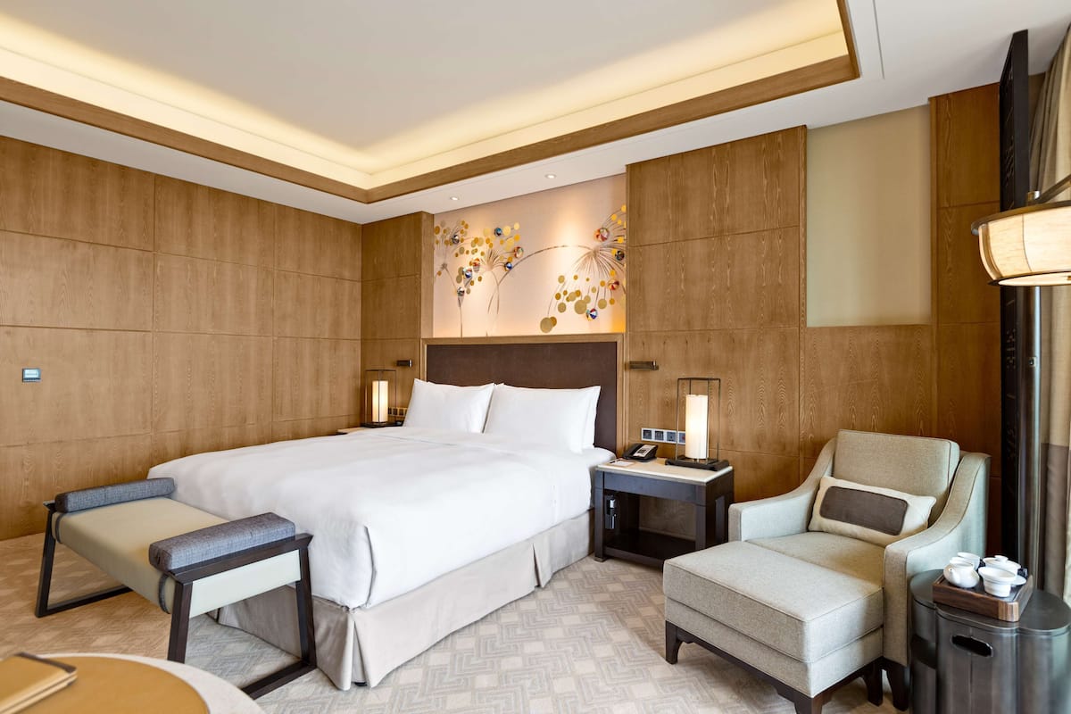 Quarto de hotel com uma cama grande, mesas de cabeceira, uma cadeira e um objeto decorativo na parede.