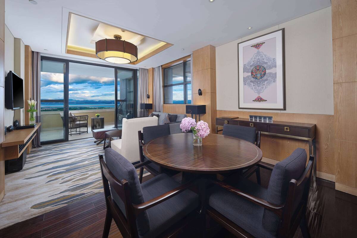 Quarto de hotel moderno com uma grande mesa redonda, assentos confortáveis, televisão de tela plana e vista para o oceano.