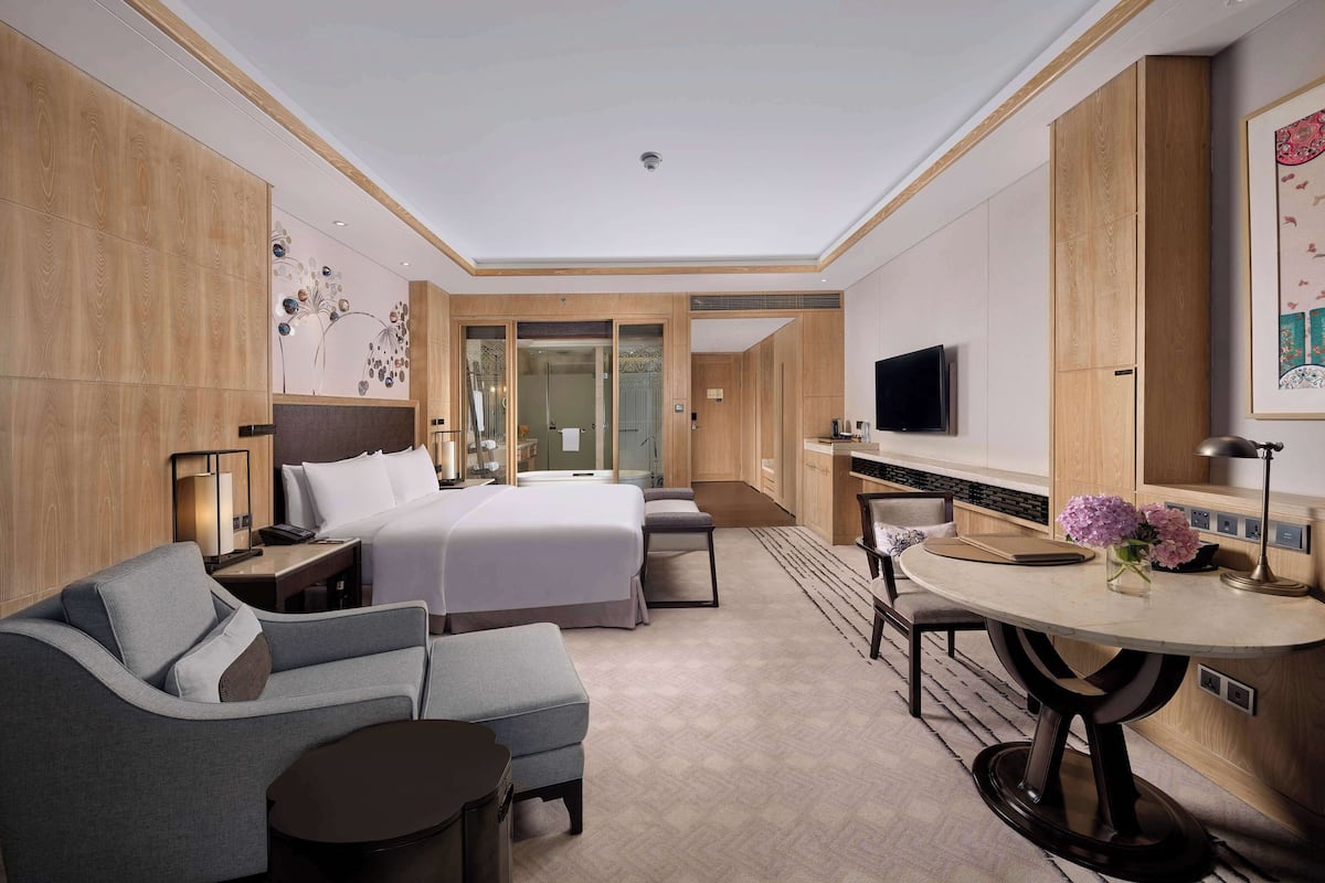 Quarto de hotel moderno com cama, sofá, mesa de jantar e televisão.