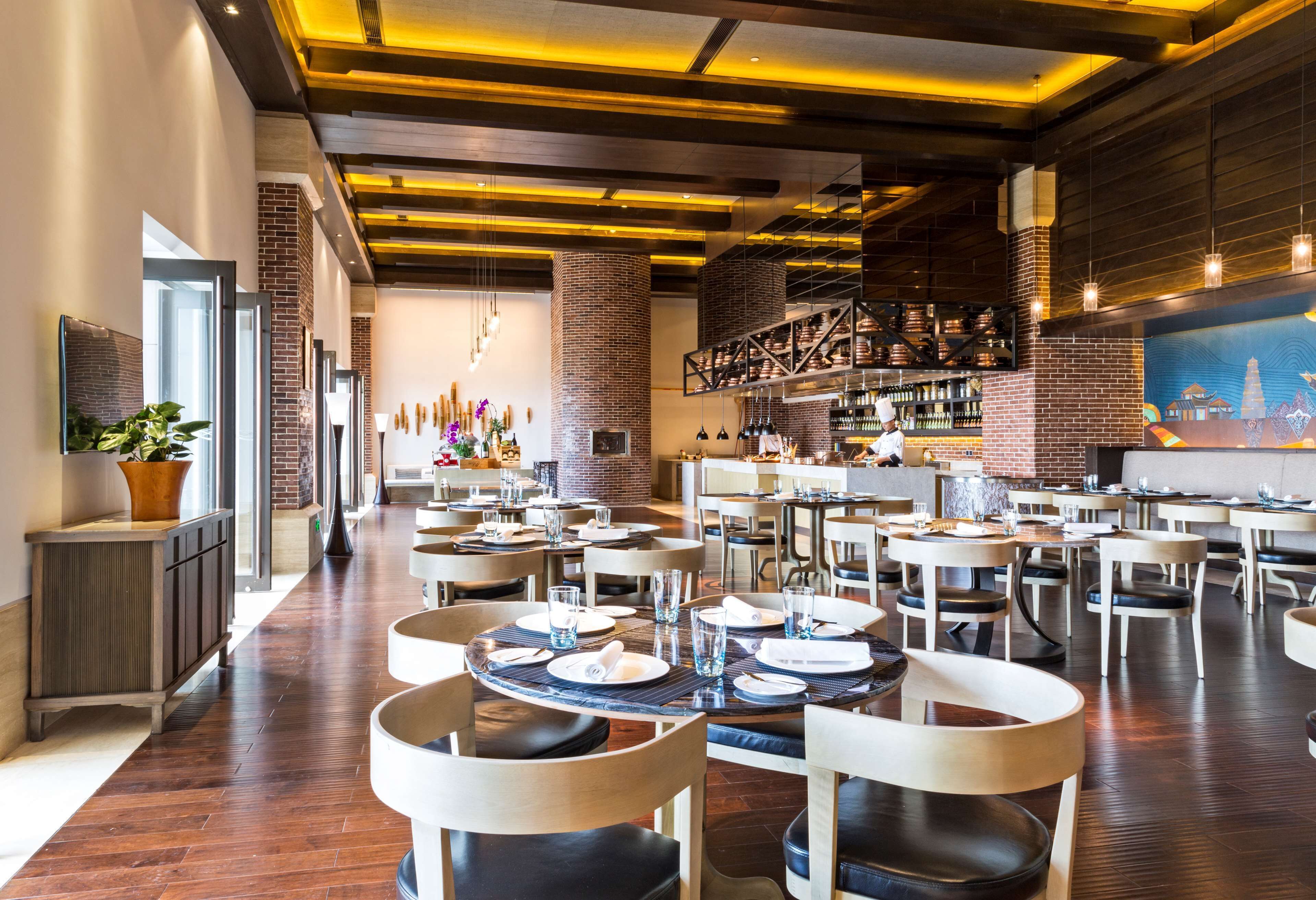 Restaurante moderno com paredes de tijolo, piso de madeira e área de bar. Mesas montadas com pratos, copos e talheres.