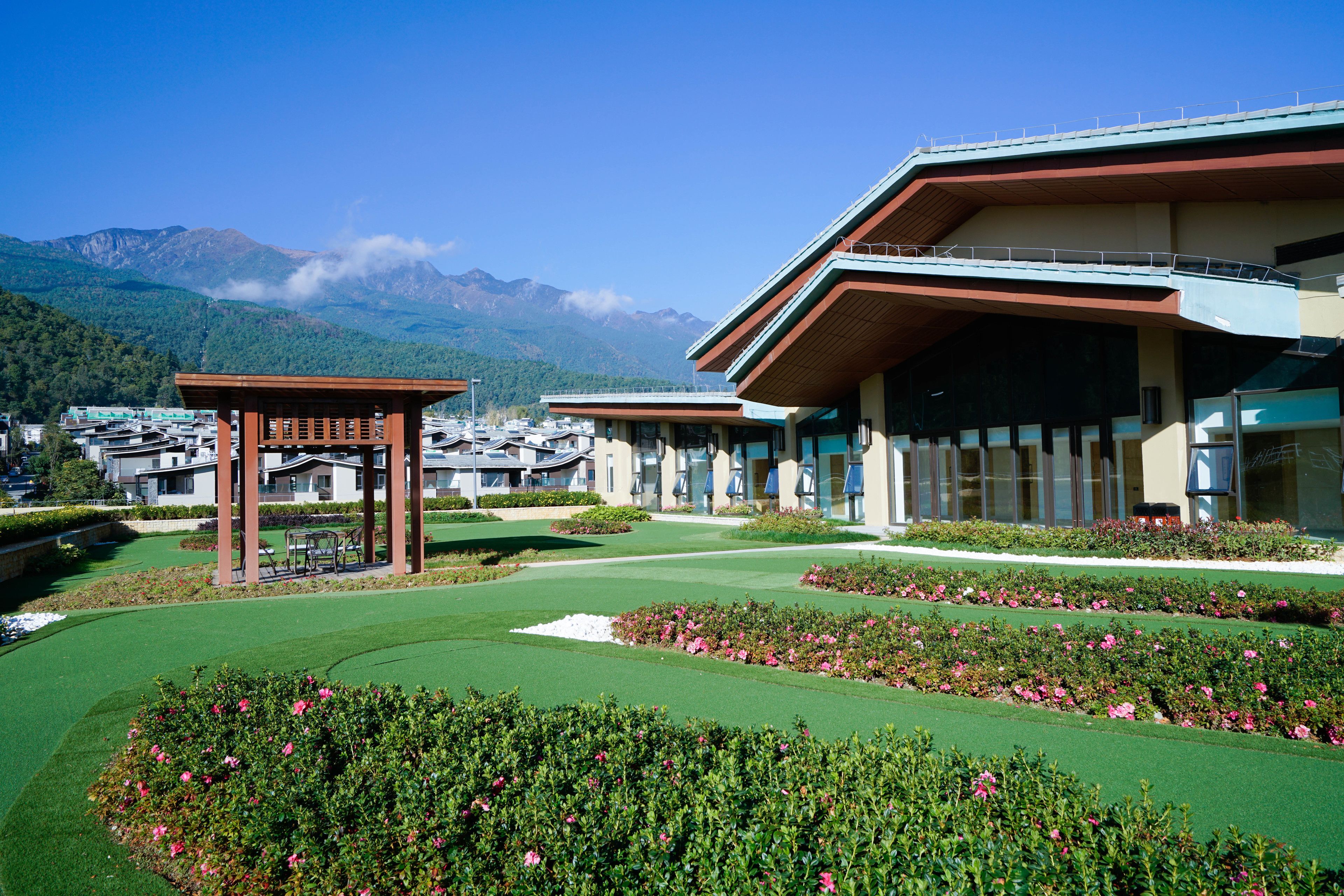 A hotel with a modern design, featuring a covered outdoor area with a pergola and a well-maintained garden with pink flowers.