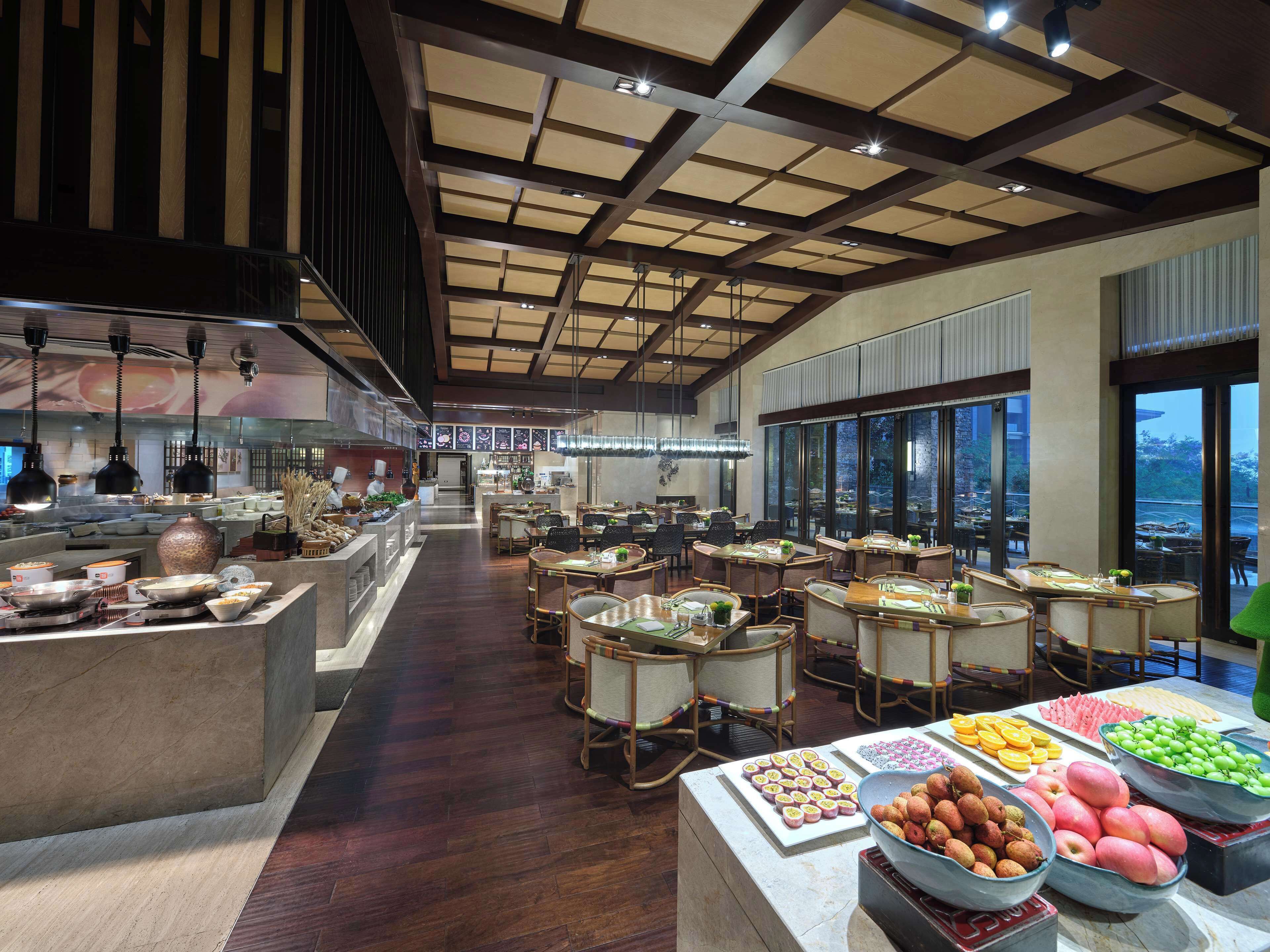 A spacious restaurant with high ceilings, a central serving area, and a buffet with various food items.