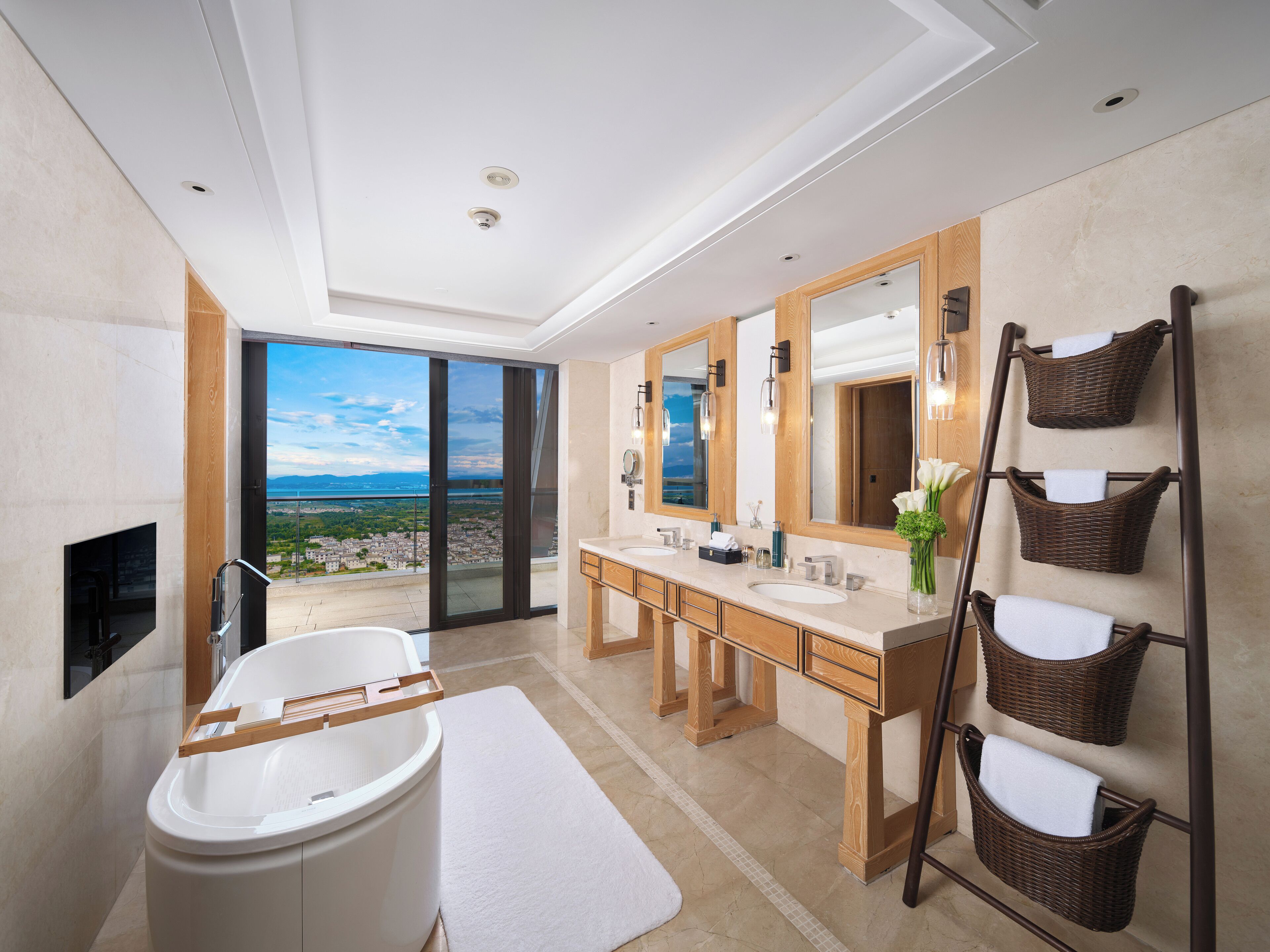 Une salle de bain moderne avec une grande baignoire, deux vasques et un grand miroir. La salle de bain offre une vue sur la ville.