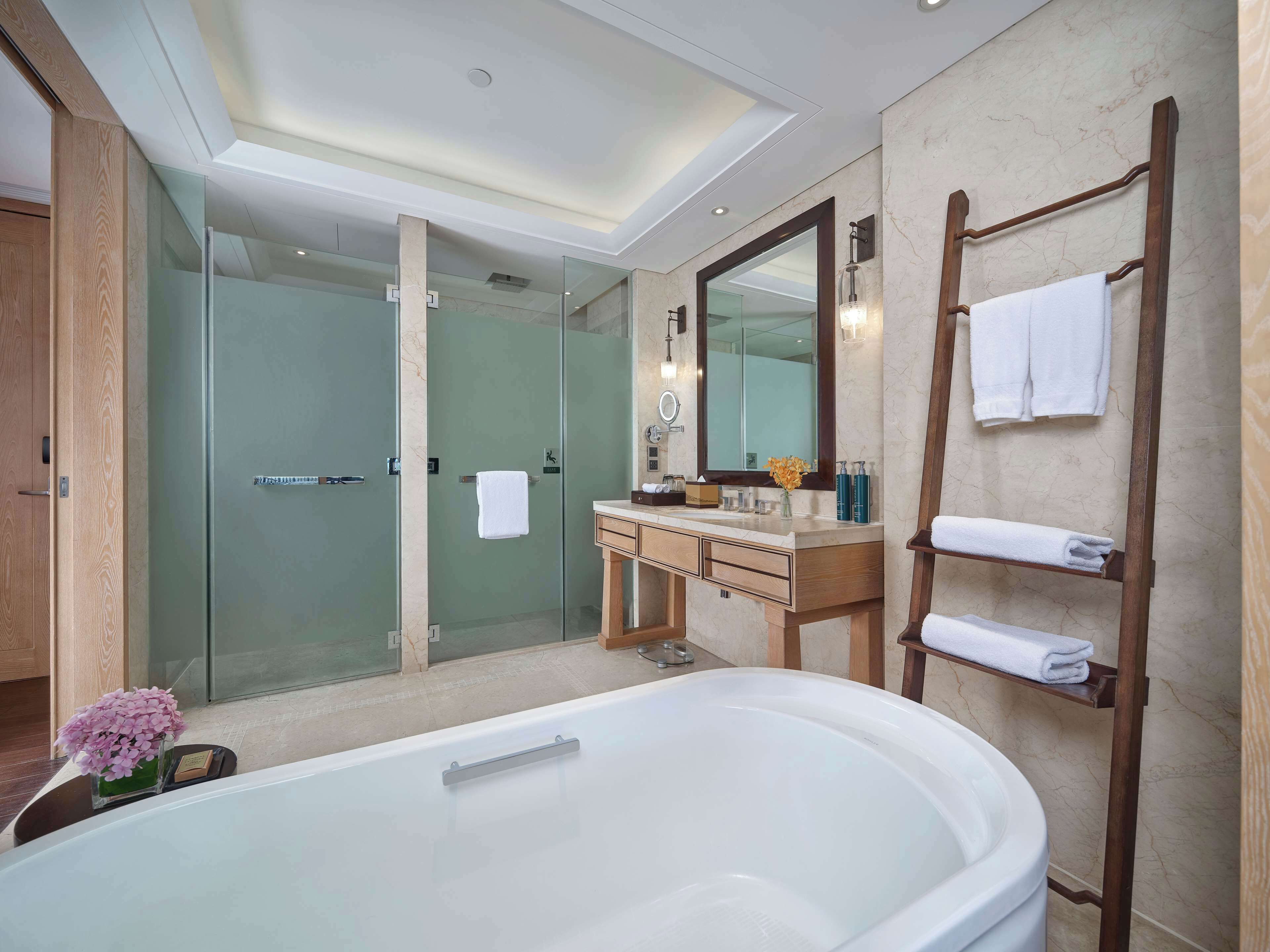 Un baño moderno con una bañera grande, ducha con mampara de vidrio y tocador con espejo y perchero.