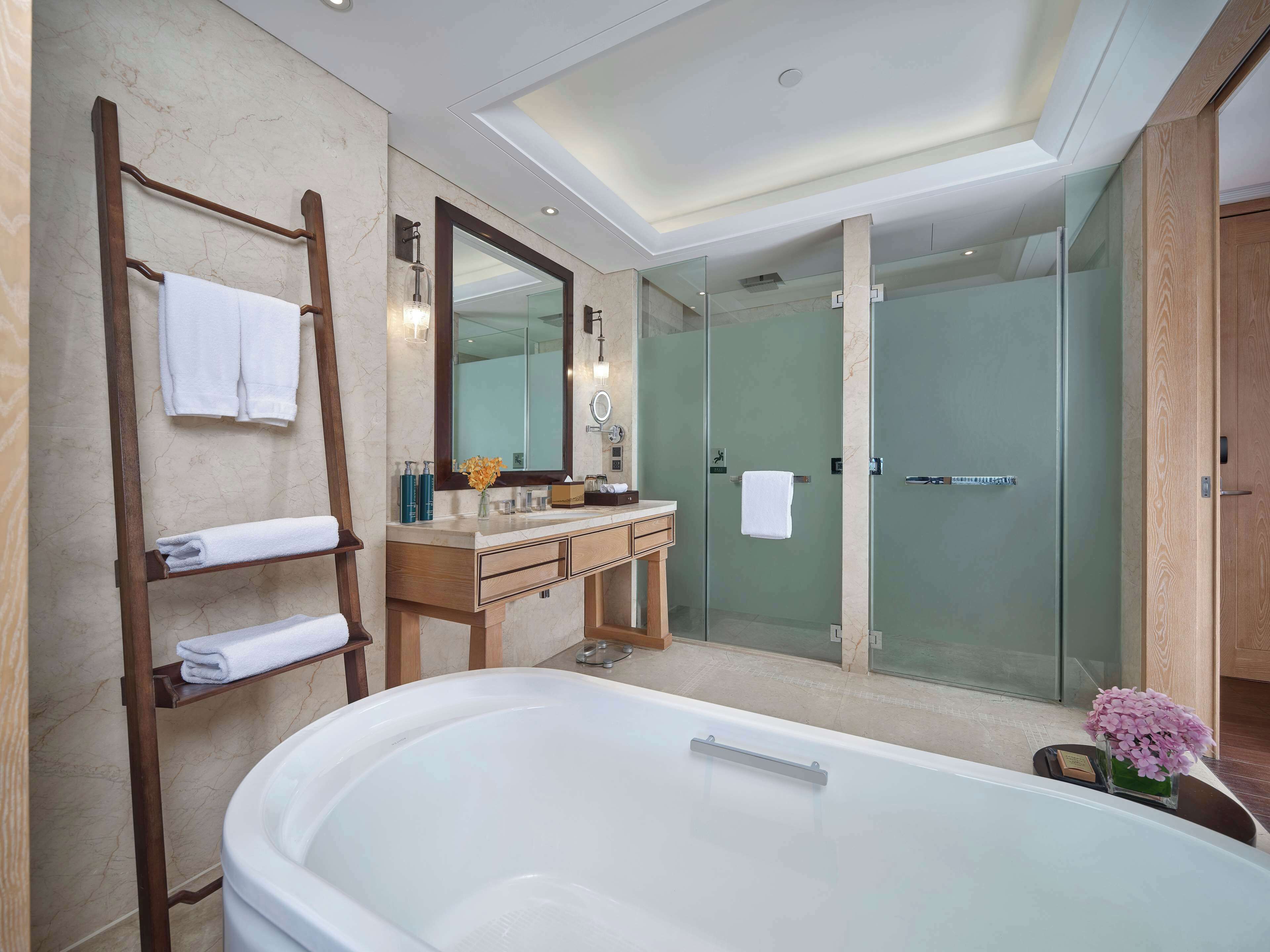 A modern bathroom with a large bathtub, a wooden vanity, a glass shower enclosure, and a towel rack with neatly folded towels.
