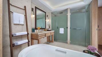 A modern bathroom with a large bathtub, a wooden vanity, a glass shower enclosure, and a towel rack with neatly folded towels.