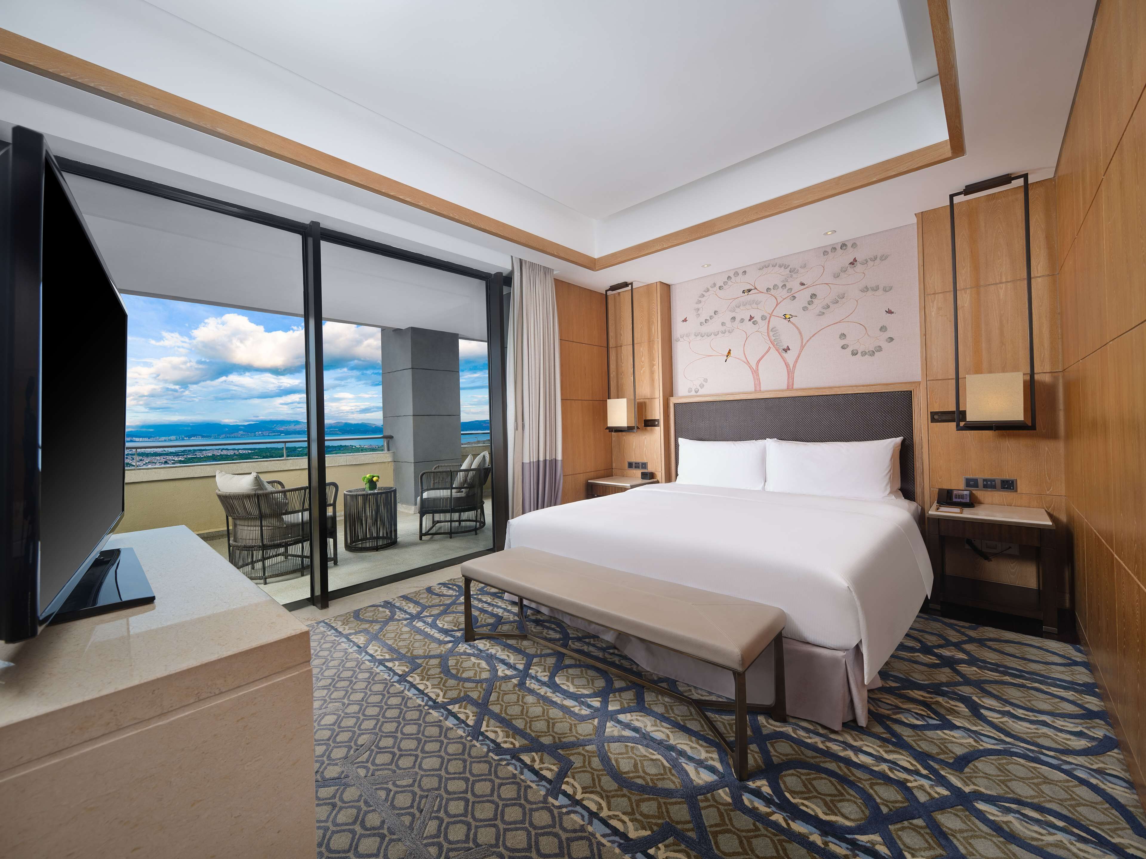 Een hotelkamer met een groot bed, een televisie, een bureau, een bankje en uitzicht op de oceaan.