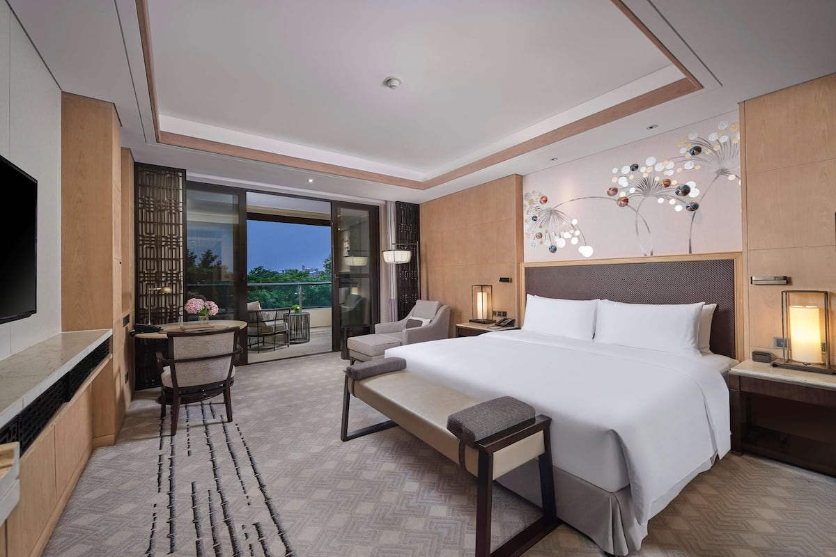 Quarto de hotel moderno com uma cama grande, uma escrivaninha com televisão, uma varanda com área de estar e um detalhe decorativo na parede.