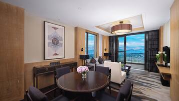 Una habitación de hotel moderna con comedor, sofá, ventana grande con vista a la ciudad y un adorno de pared decorativo.