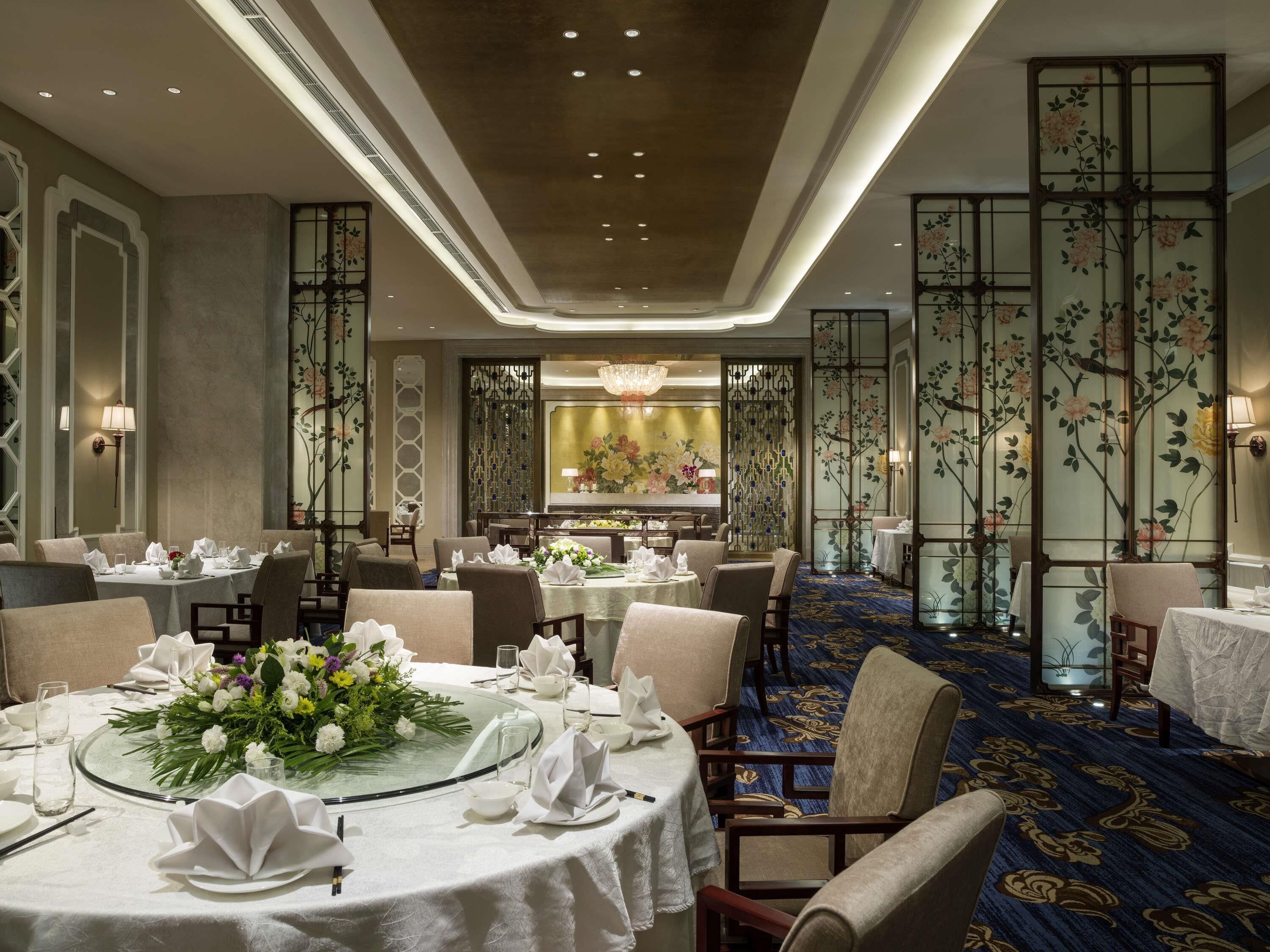 Un comedor de hotel con mesas redondas, sillas y centros de mesa florales.