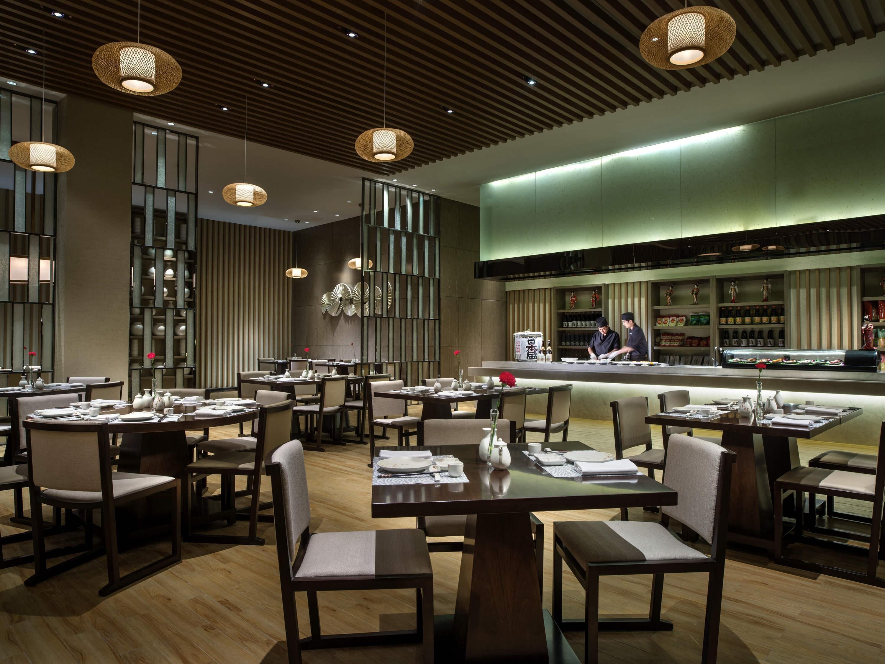 Un restaurante moderno con suelos de madera, mesas redondas e iluminación colgante.