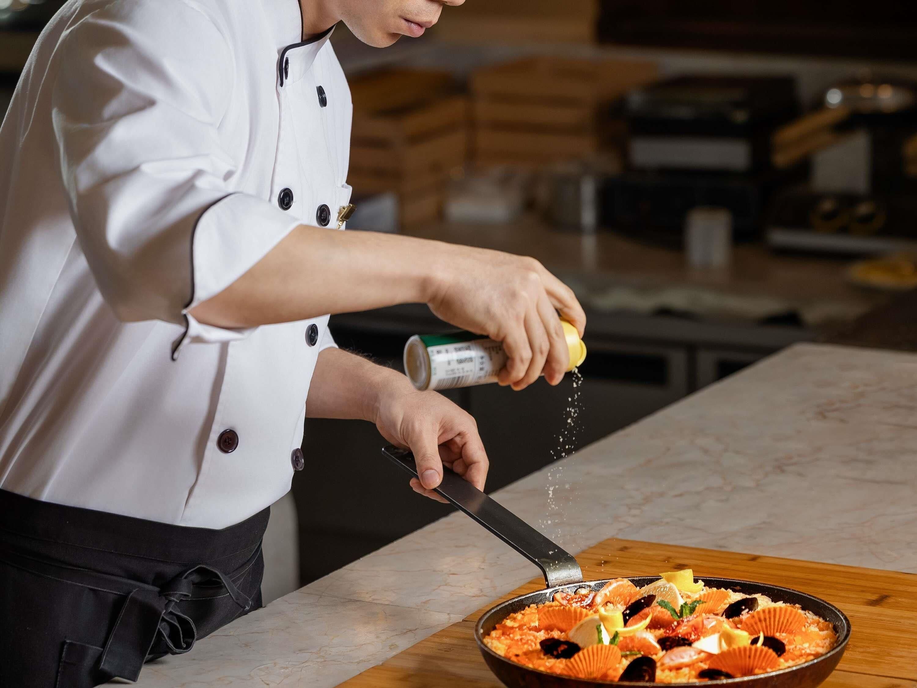 Un chef sazonando un plato en una cocina.