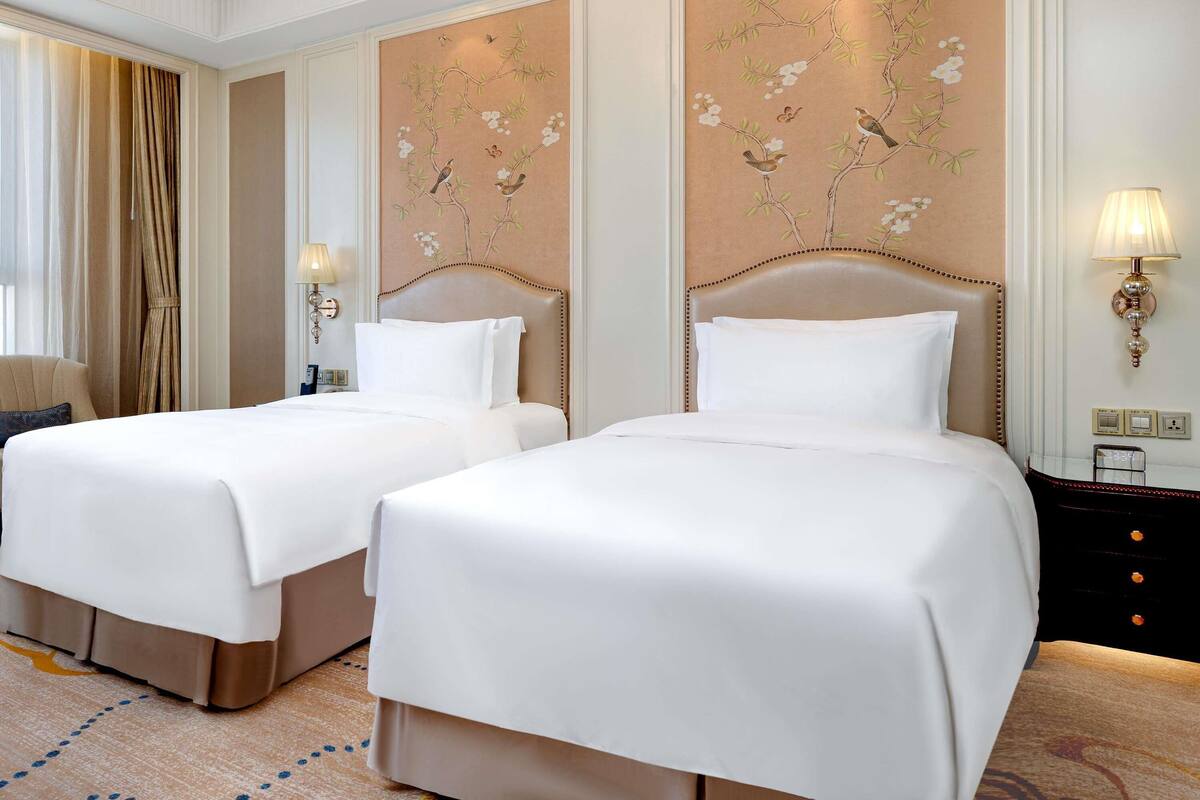 A hotel room with two beds, a chandelier, and a wall with floral artwork.