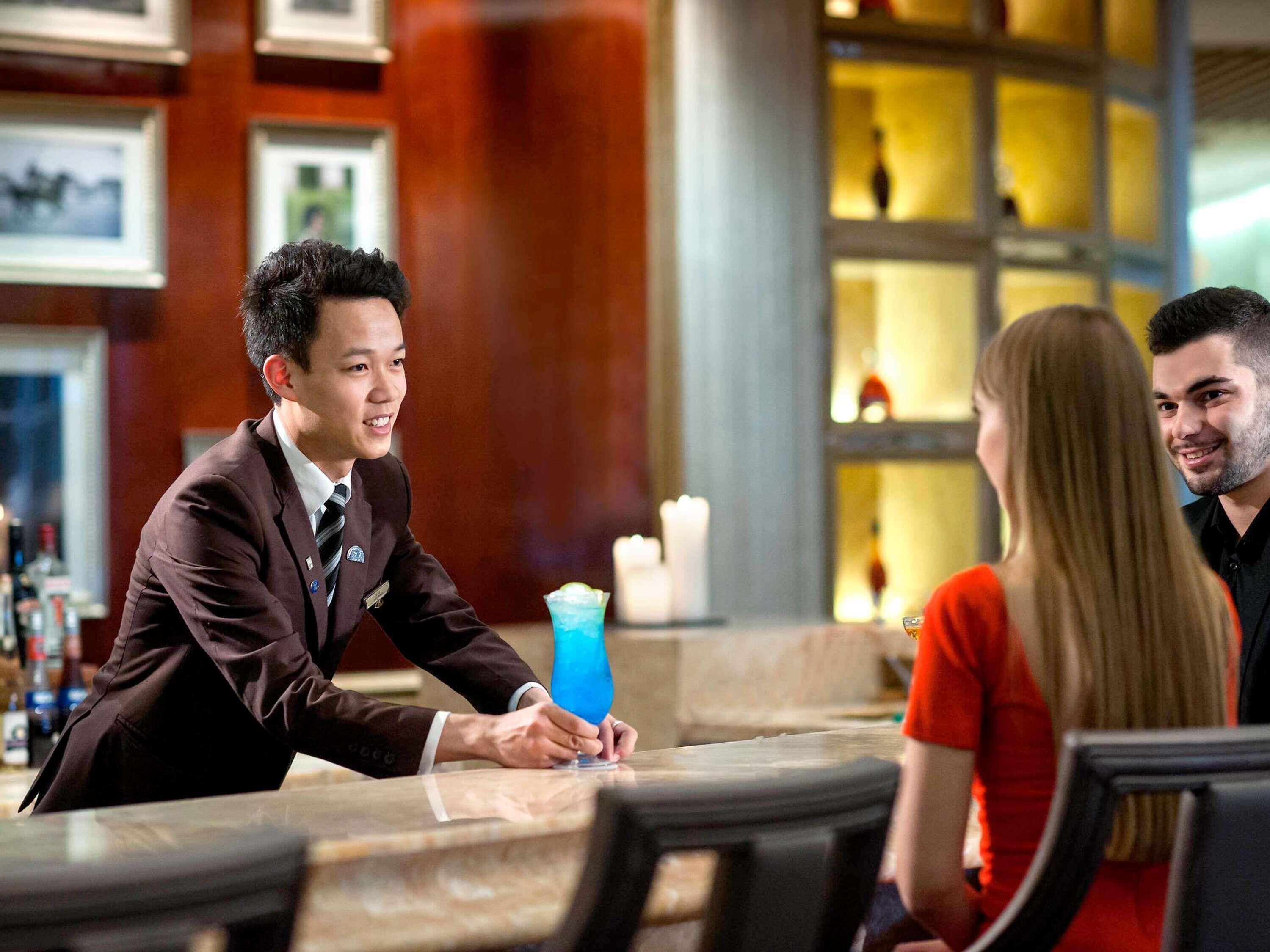 A bar area with a bartender, a table, and a drink.